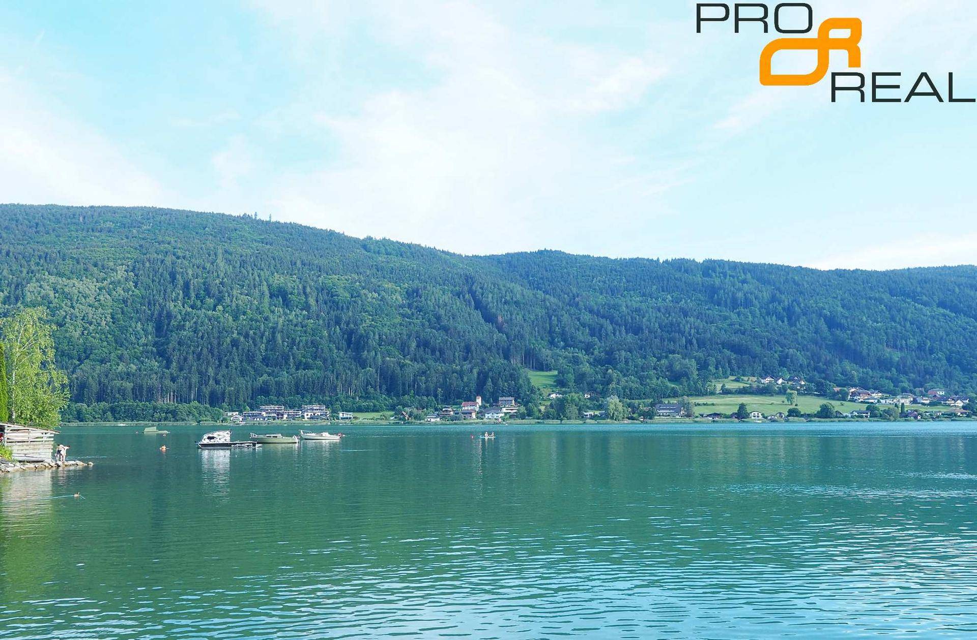 Panoramablick auf einen ruhigen See, umgeben von dichten Wäldern und einem malerischen Dorf am Ufer.
