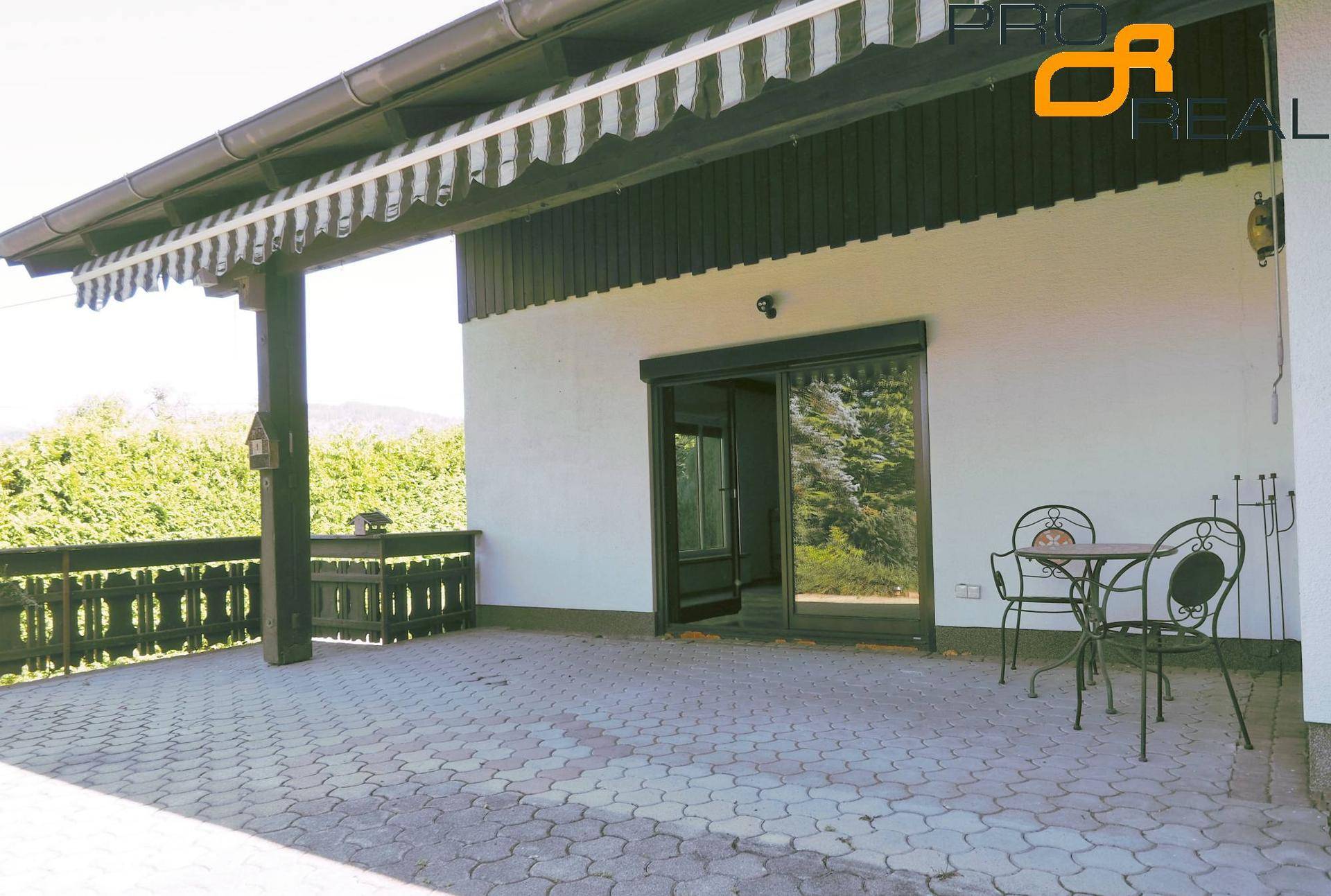 Geräumige, gepflasterte Terrasse mit Markise und Gartenmöbeln, ideal für Entspannung im Freien.