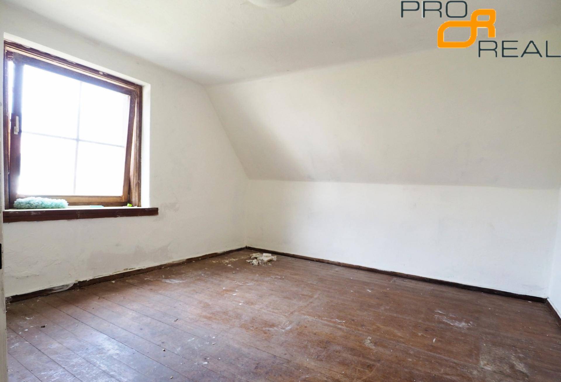 Helles Dachzimmer mit schrägen Wänden, Holzboden und einem Fenster.