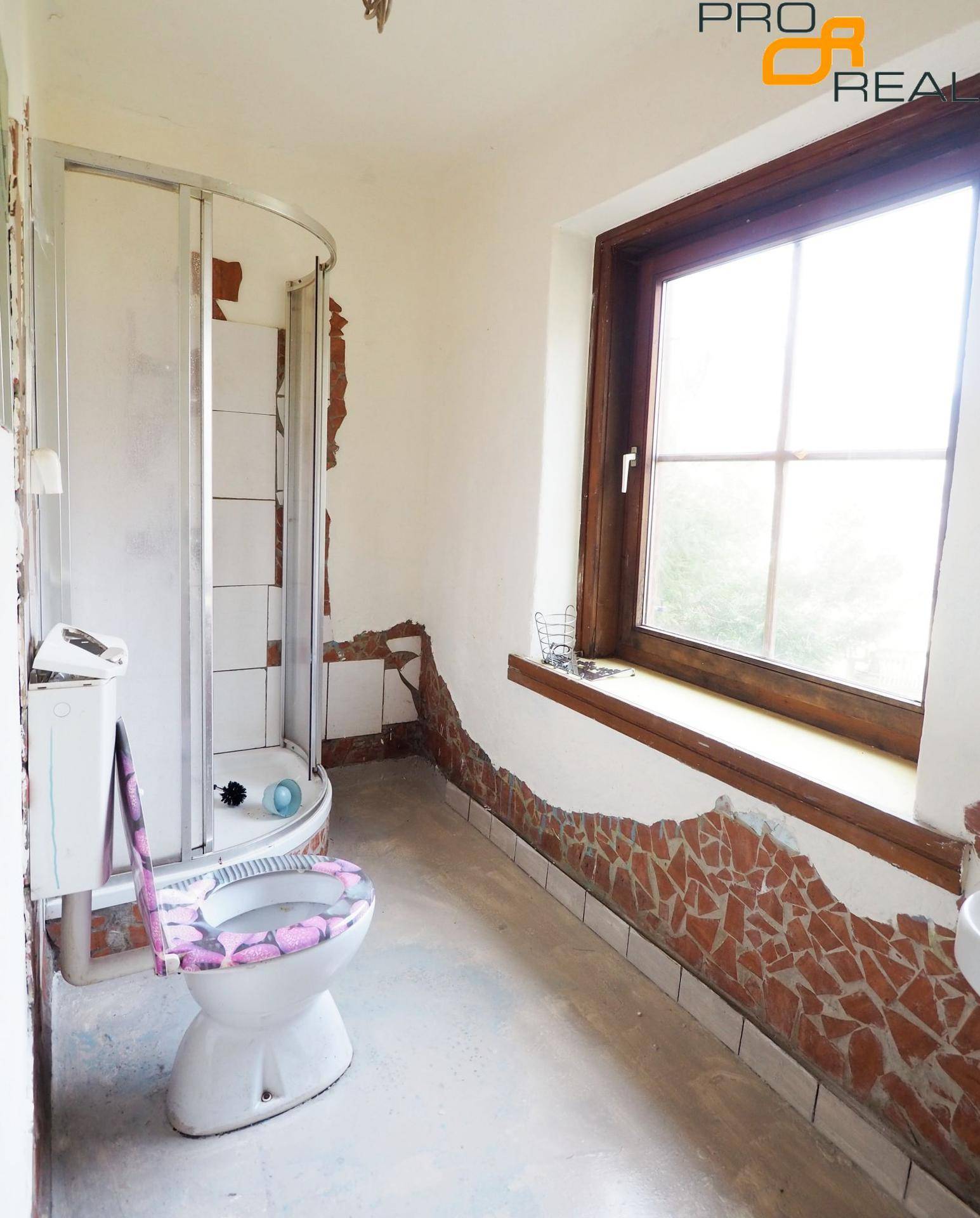 Badezimmer mit Dusche, Toilette und einem großen Fenster, das viel Licht spendet.
