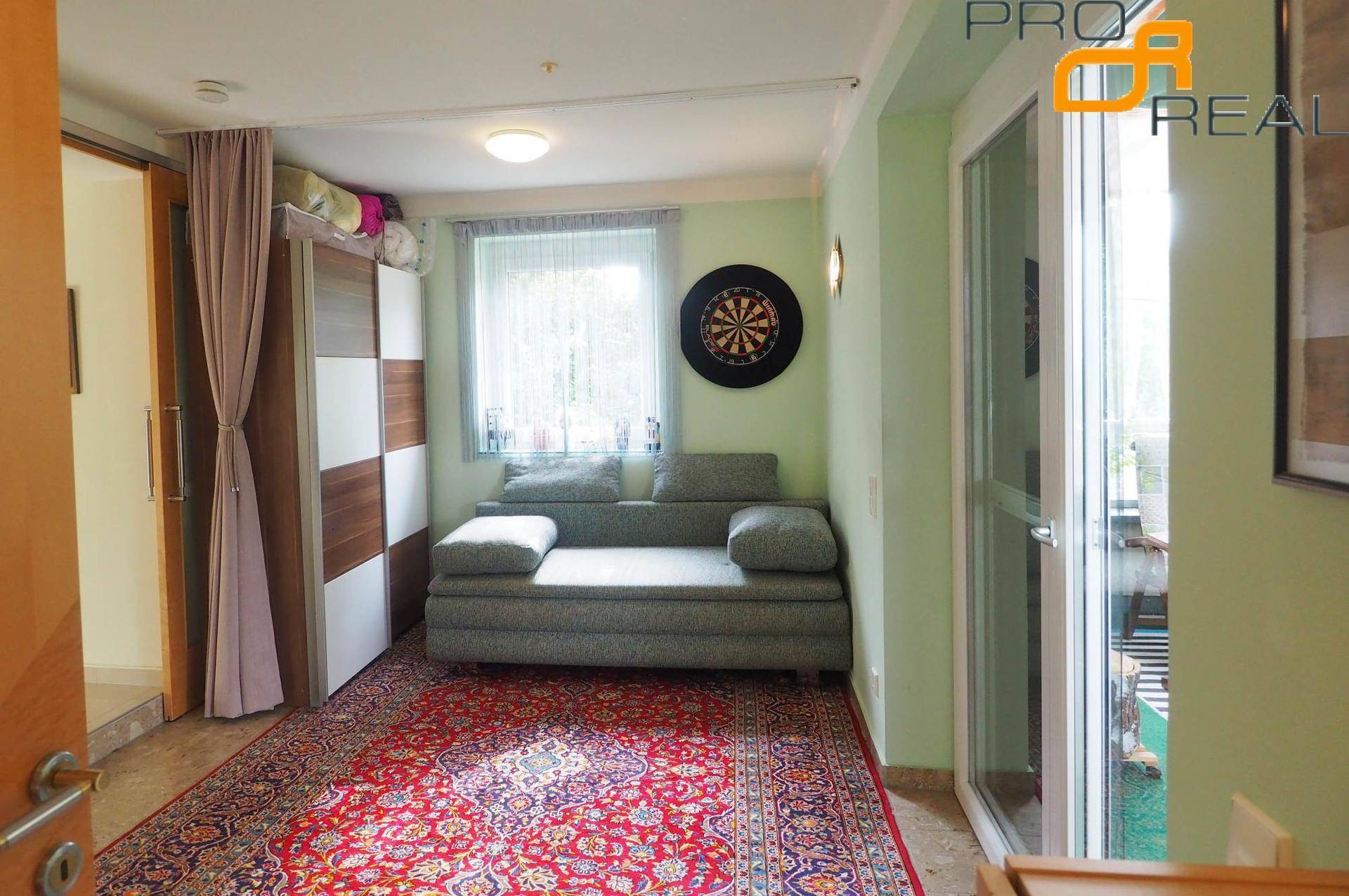 Gemütlicher kleiner Raum mit Sofa, Fenster und Dartscheibe an der Wand, ausgelegt mit einem Teppich.