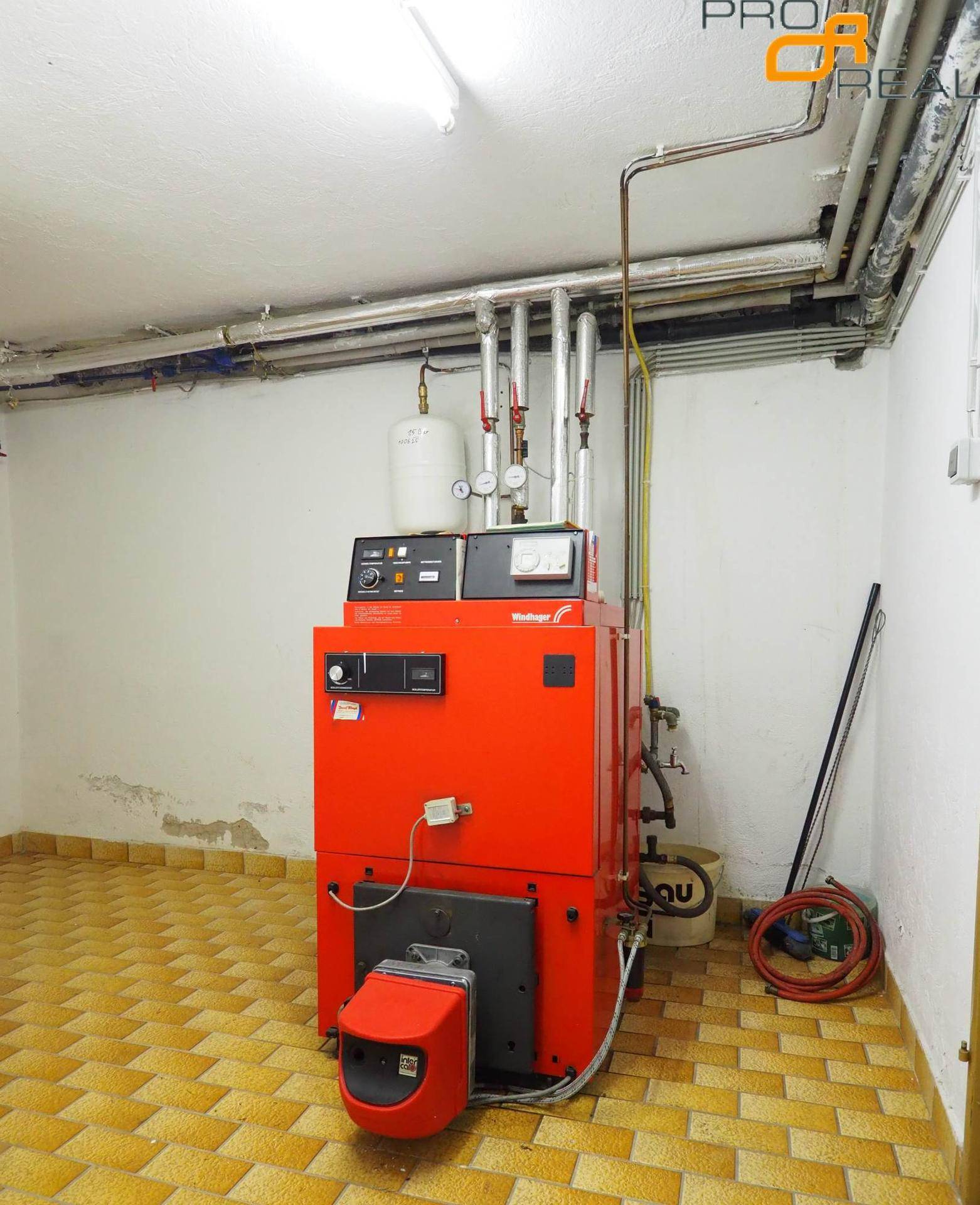 Heizungsraum im Keller mit einem großen roten Heizkessel und sichtbaren Rohren.