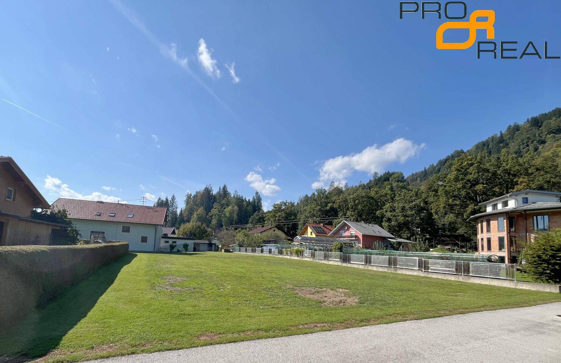 Großes Grundstück mit Rasenfläche und Hecke, umgeben von Wohnhäusern und einer malerischen Berglandschaft.