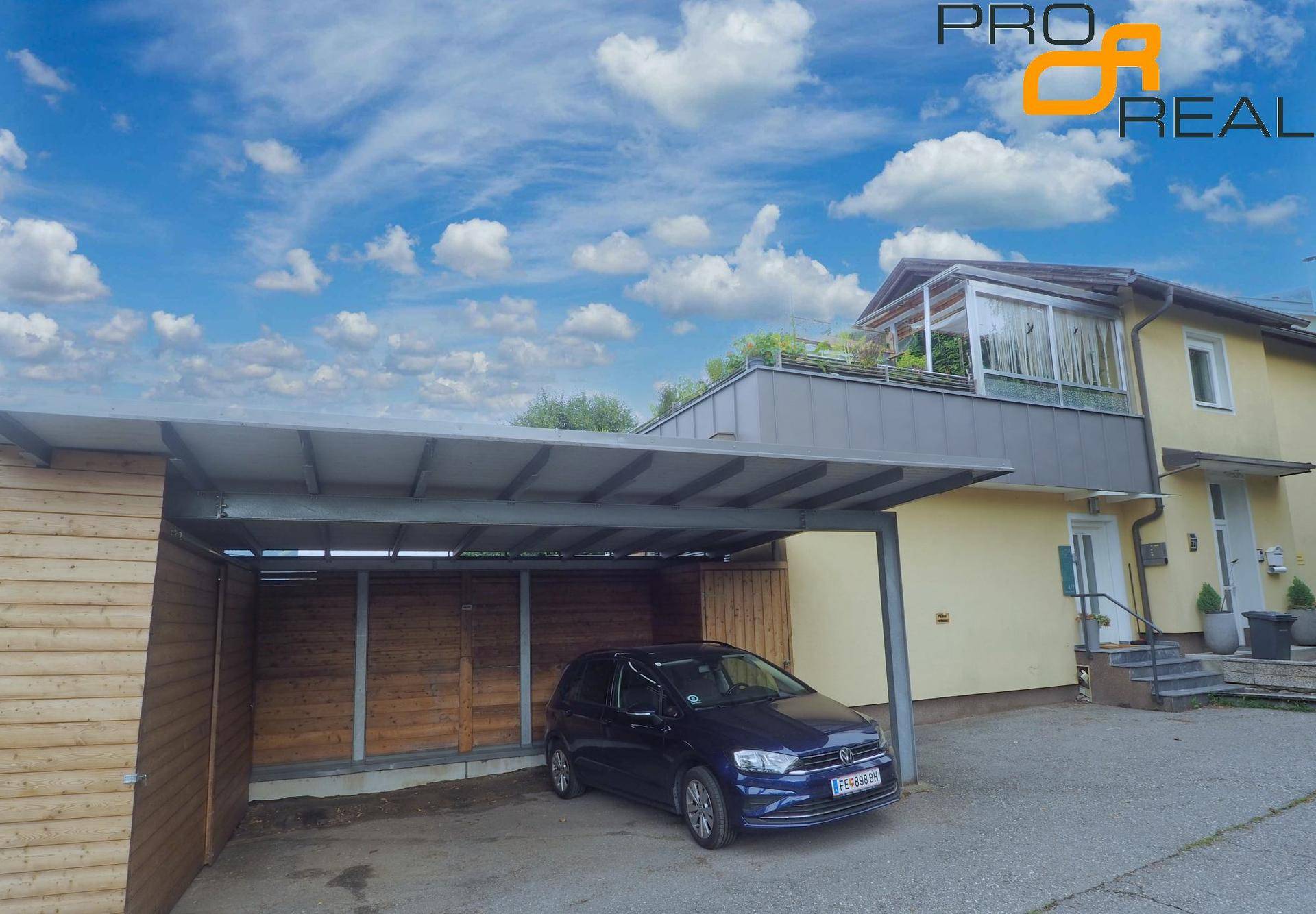 Überdachter Carport neben einem Wohnhaus mit einem geparkten Auto und blauem Himmel.