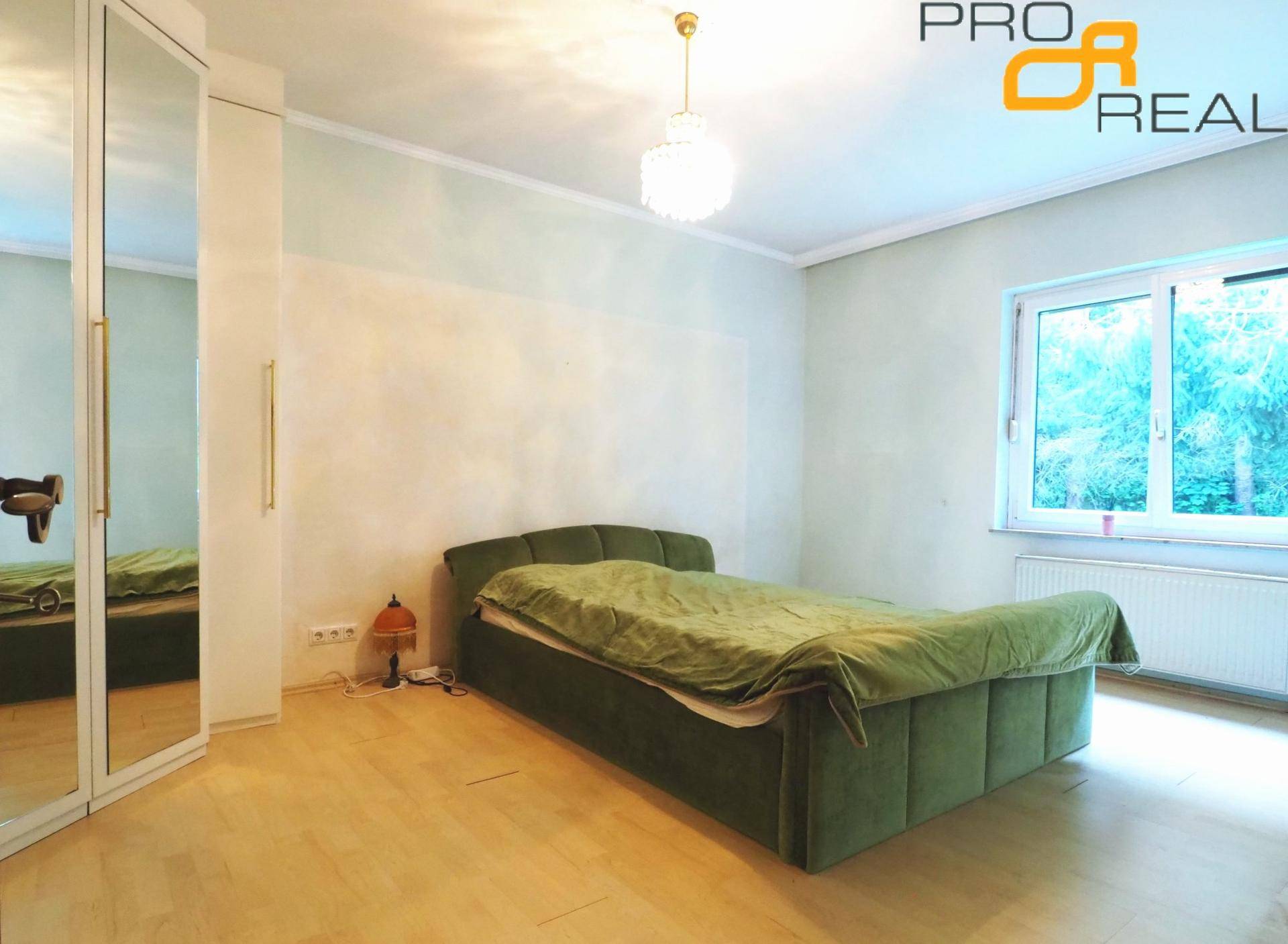 Schlafzimmer mit grünem Bett, Spiegelschrank und Fenster mit Blick ins Grüne.