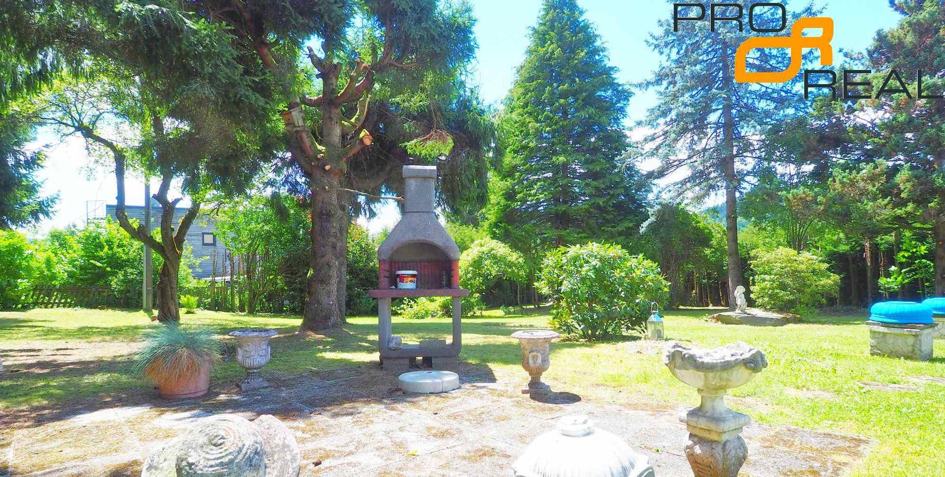 Gartenbereich mit festem Grillplatz, dekorativen Elementen und schattenspendenden Bäumen.