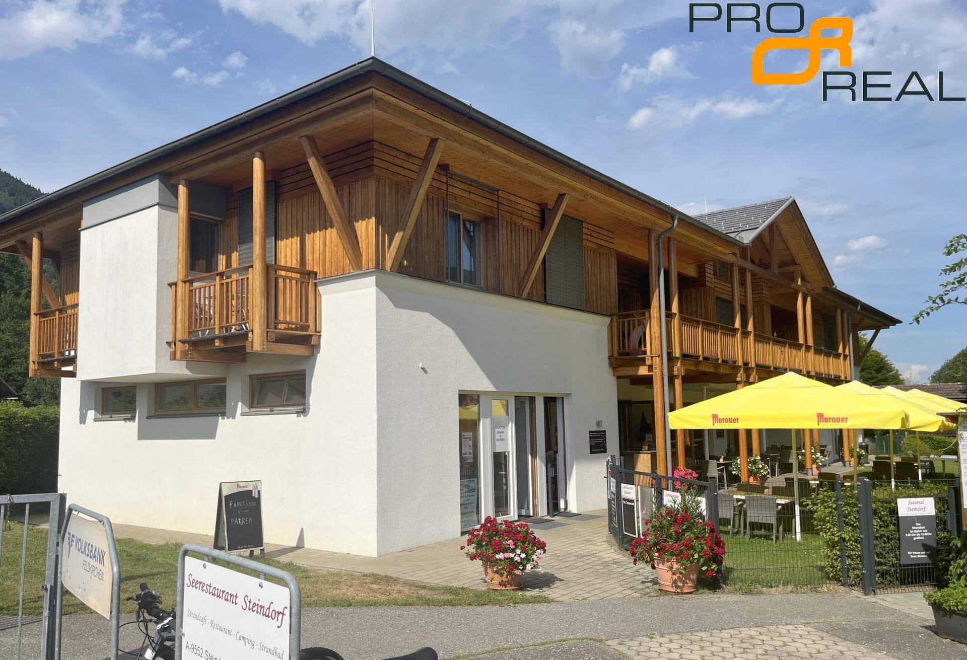 Modernes Gebäude mit Holzfassade, weißem Putz und Außenbereich eines Restaurants.