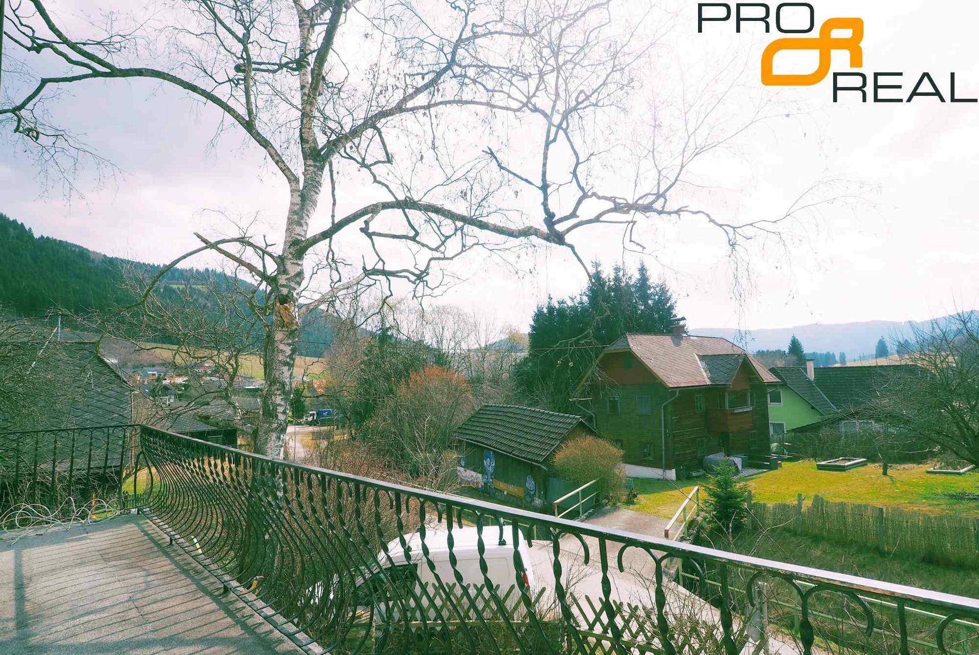 Balkon mit schmiedeeisernem Geländer und weitem Blick auf die grüne Landschaft und Berge.