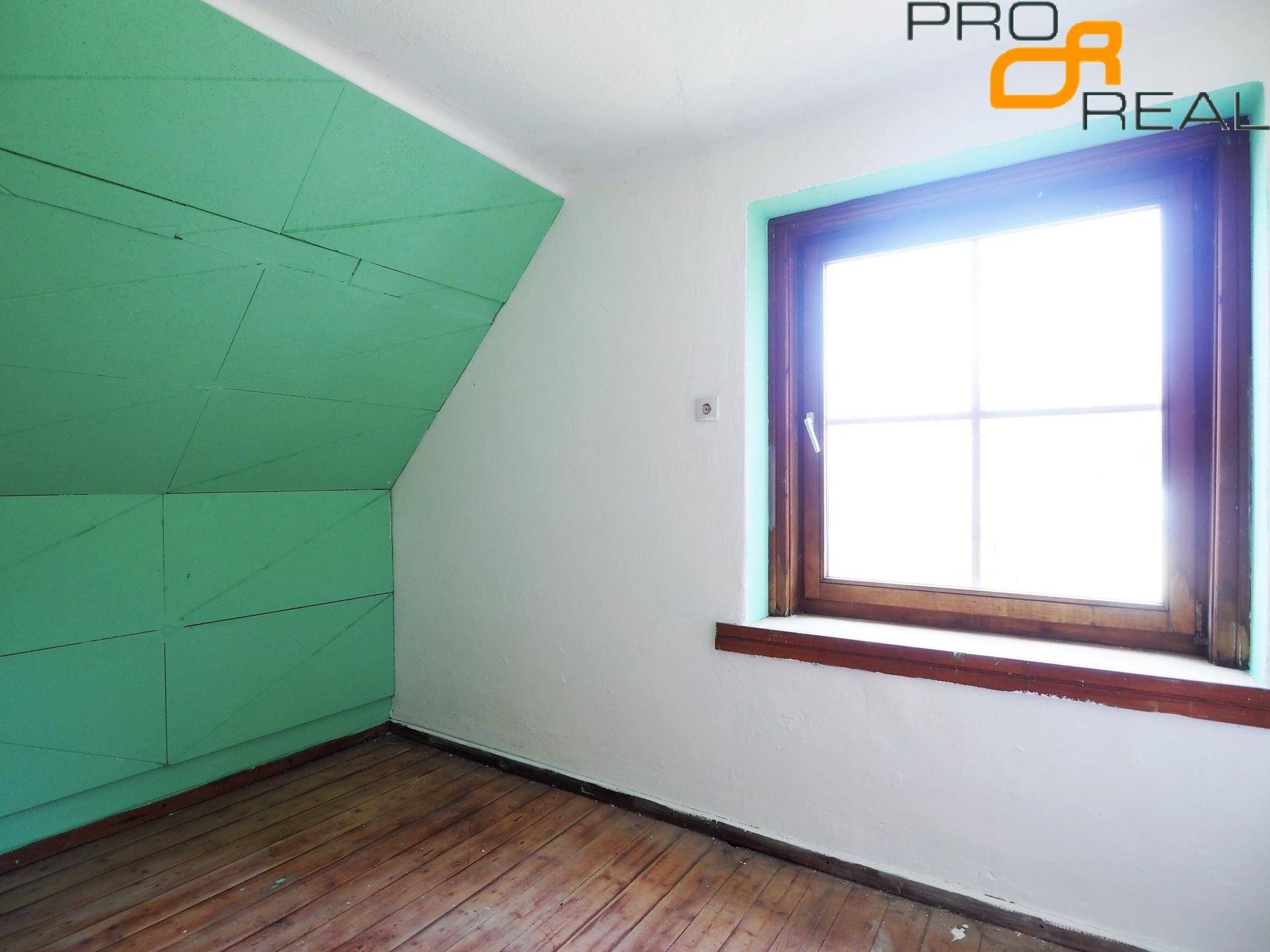 Dachzimmer mit schrägen Wänden, Holzboden und einem Fenster, das Tageslicht hereinlässt.
