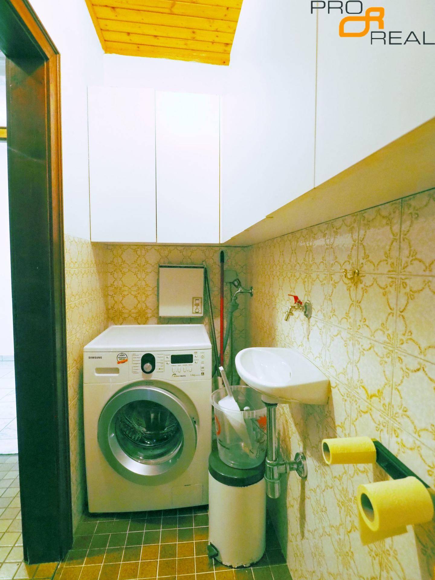 Hauswirtschaftsraum mit Waschmaschine, kleinem Waschbecken und gemusterten Wandfliesen.