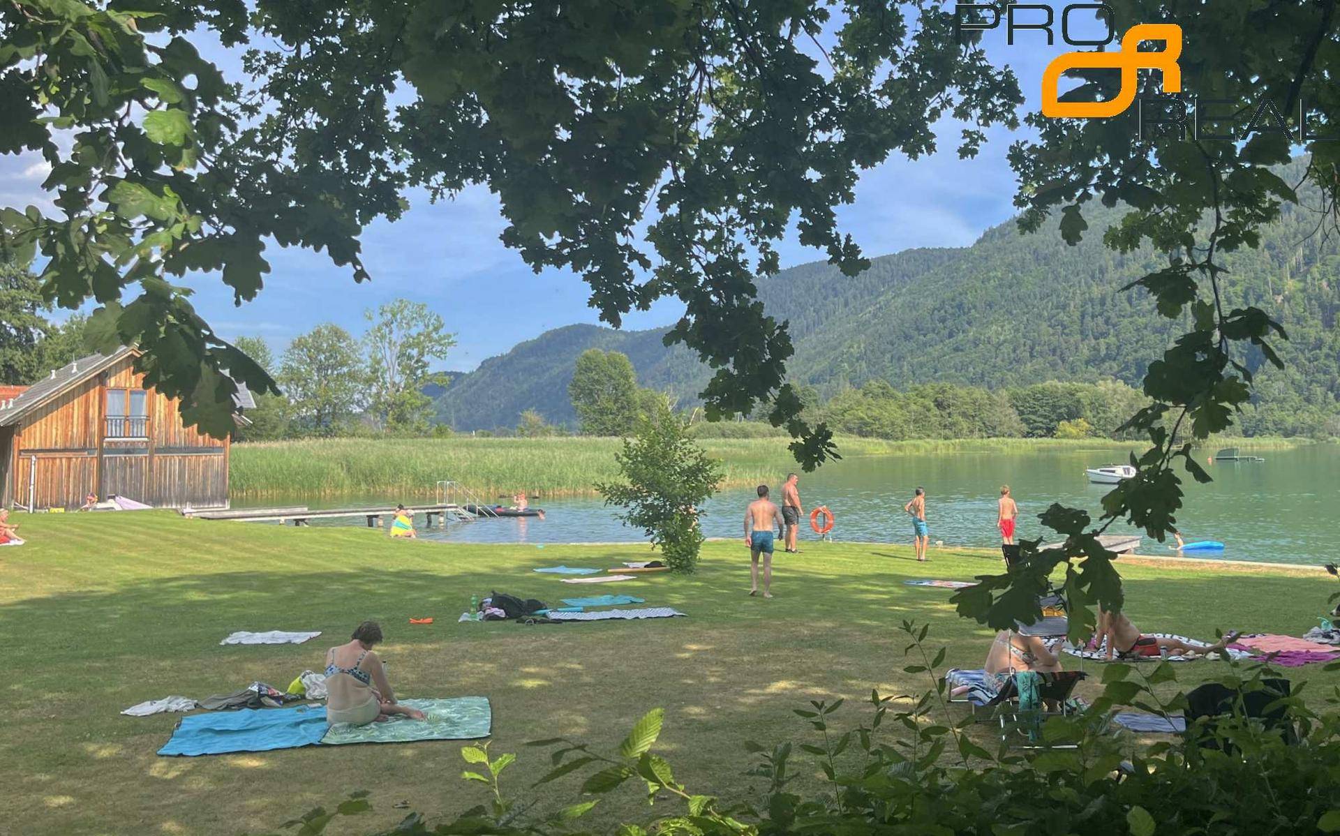 Erholungsbereich am Seeufer mit Badegästen, Steg und malerischem Bergpanorama.