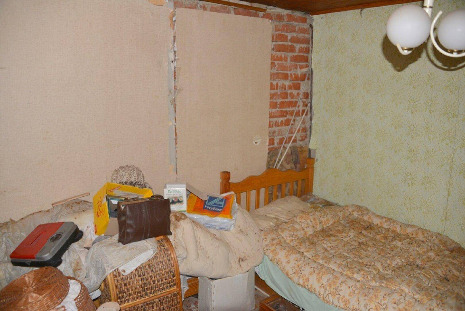 Unaufgeräumtes Schlafzimmer mit freigelegten Ziegelwänden und älterer Tapete, die Renovierung benötigt.