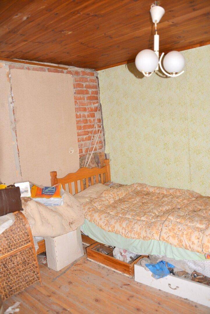 Schlafzimmer mit Holzboden, freigelegten Ziegeln und einfacher Einrichtung, die Renovierung benötigt.