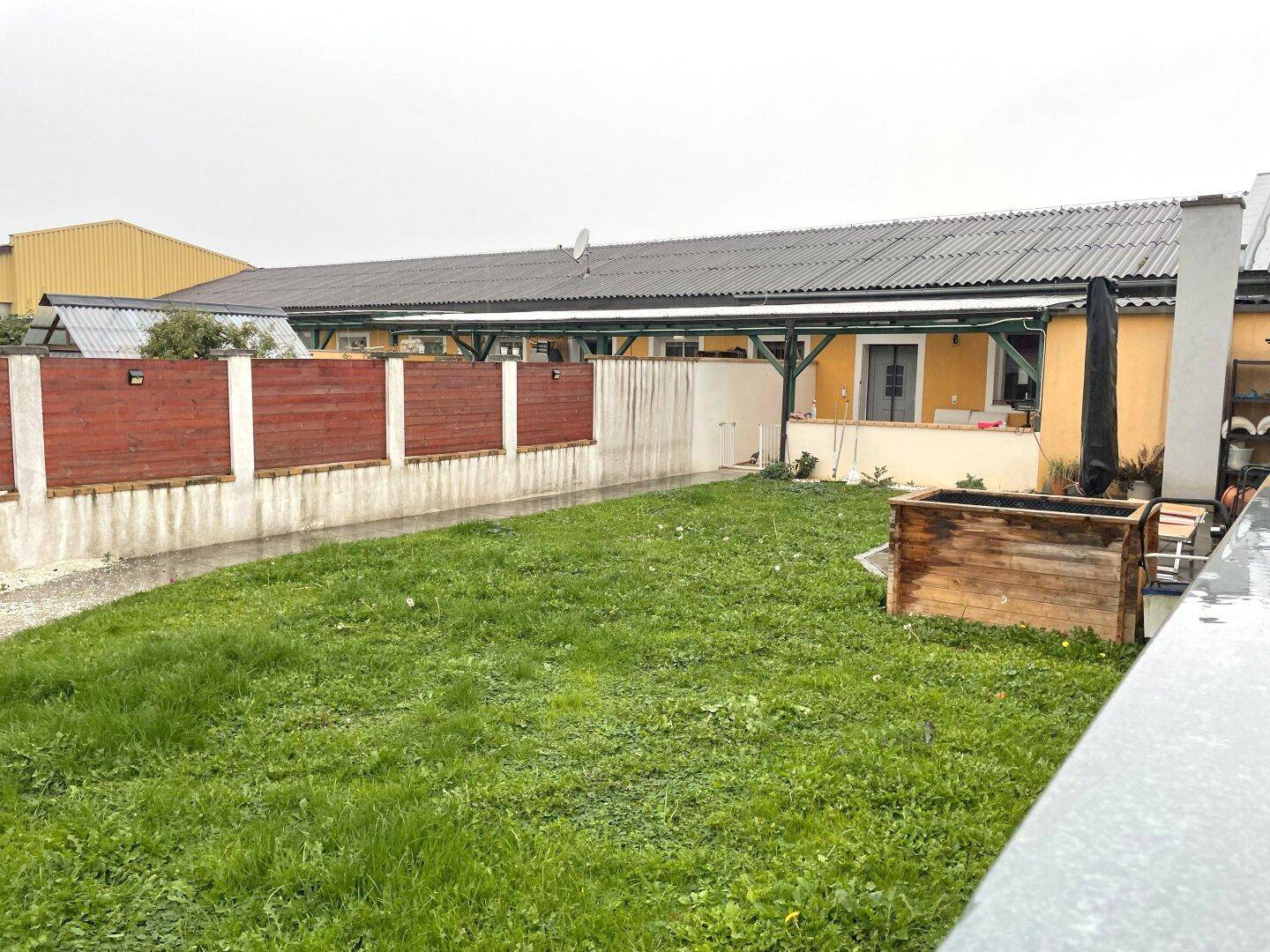 Hinterhof mit Rasenfläche, einer erhöhten Holzpflanzkiste und einer überdachten Terrasse.