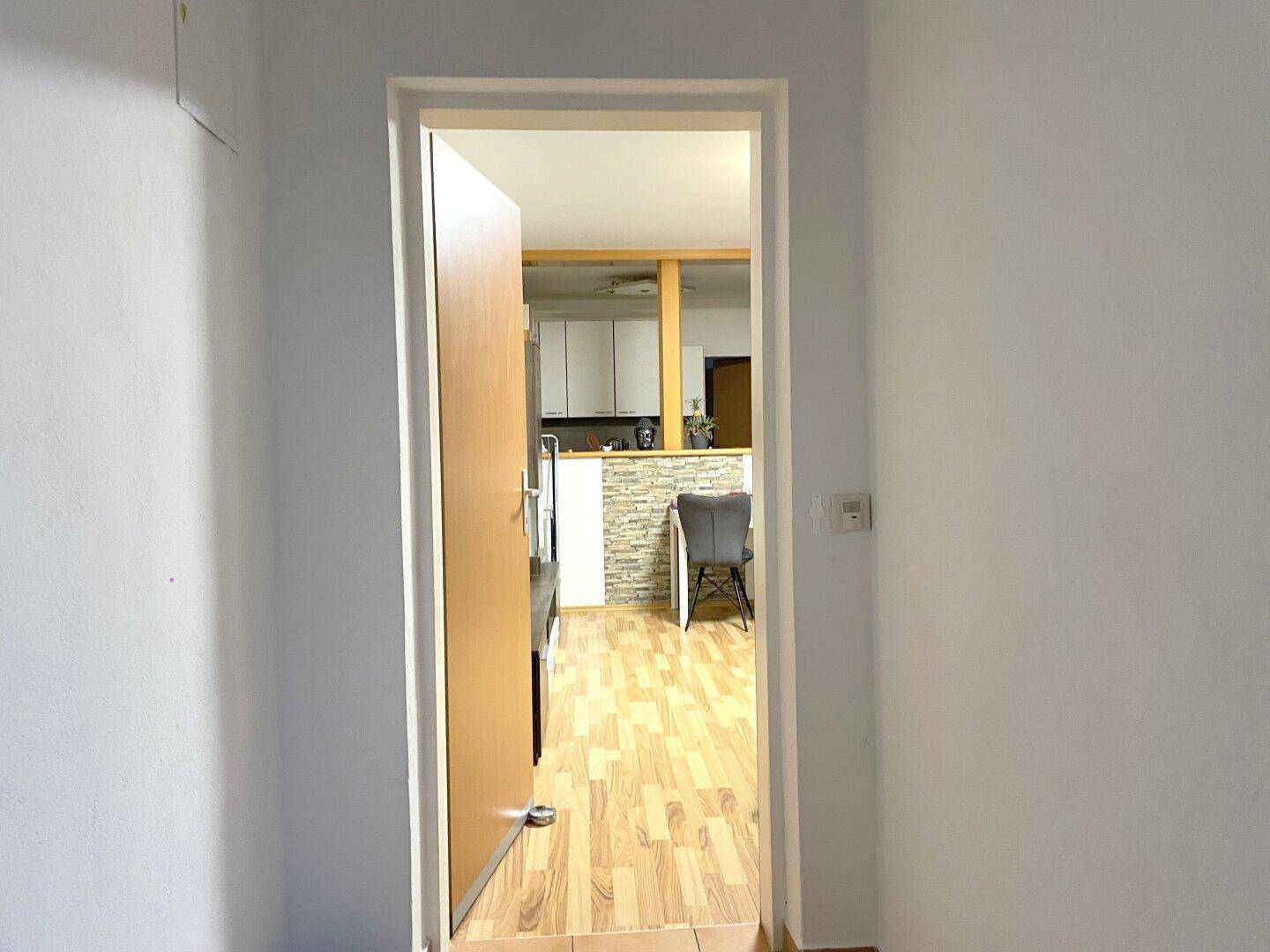 Heller Flur mit Holztür, der den Blick auf einen offenen Wohnbereich mit Küche freigibt.