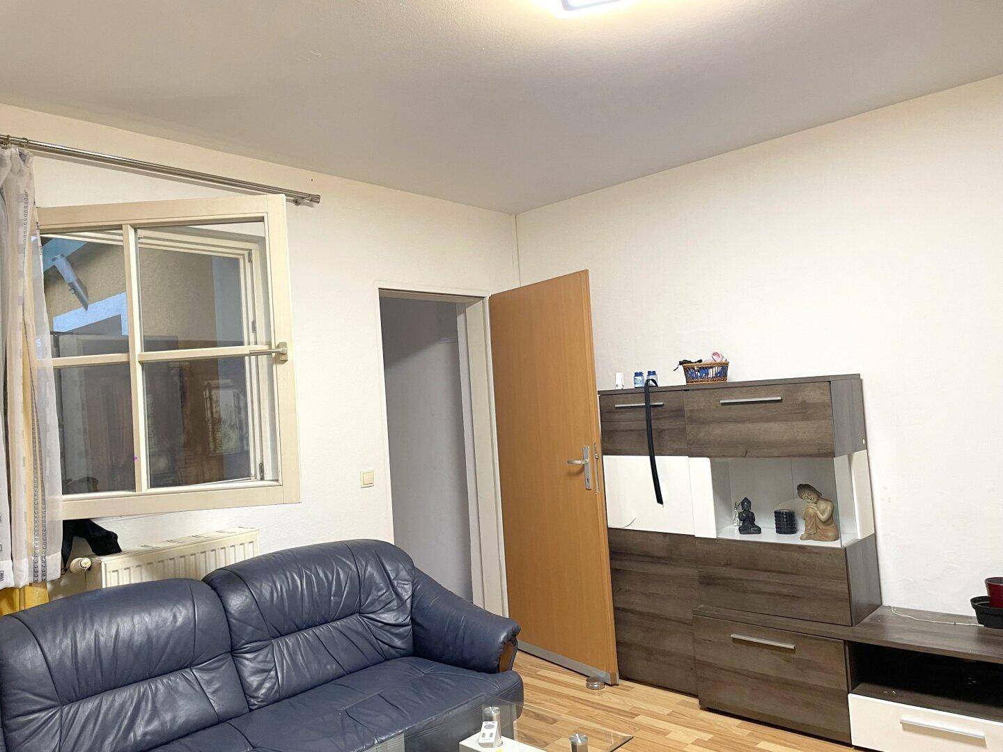 Gemütliches Wohnzimmer mit blauem Ledersofa, Holzboden und einem geöffneten Fenster.