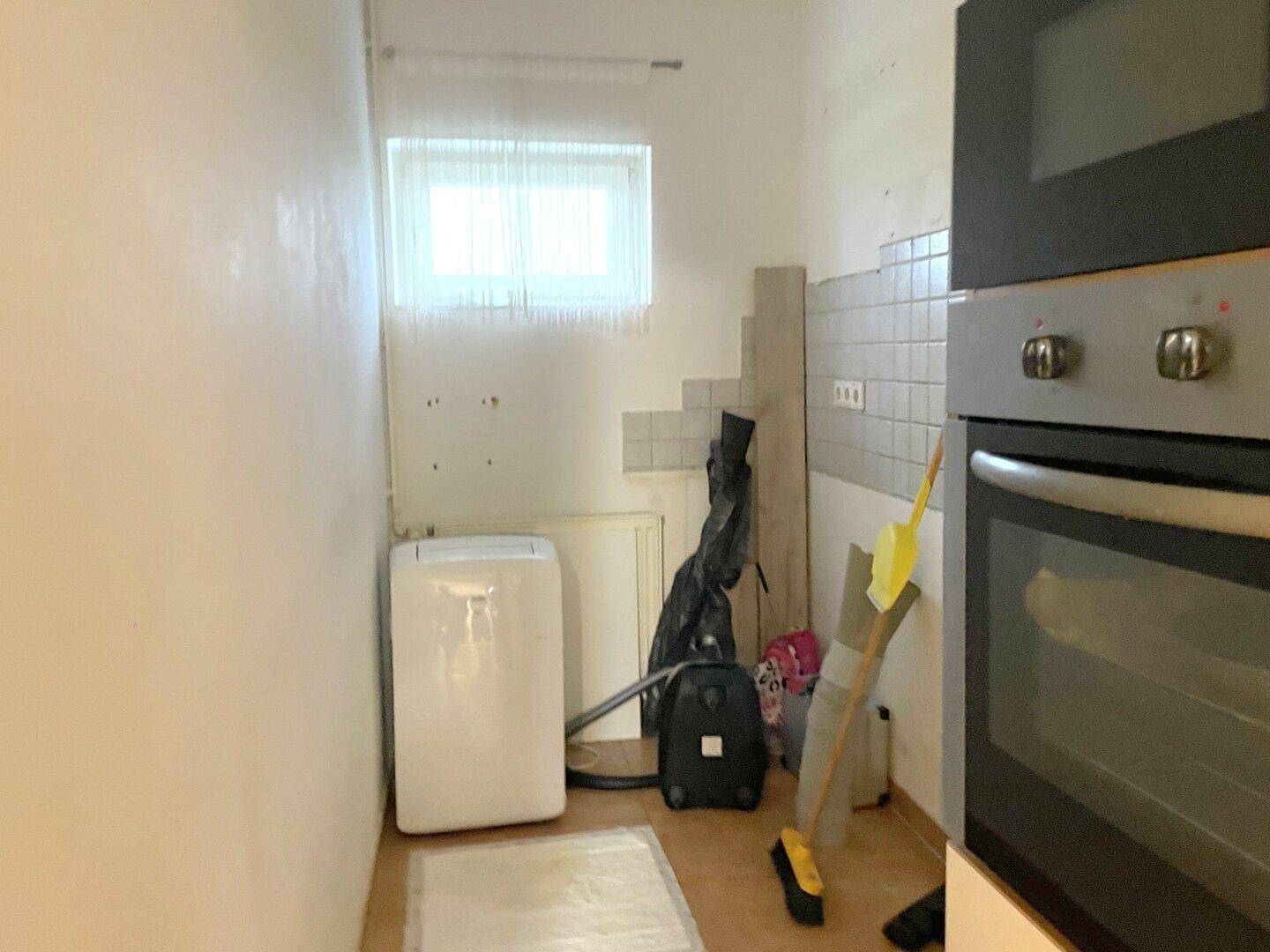 Kleiner Hauswirtschaftsraum mit Fenster, Einbaubackofen und Fliesen an der Wand.