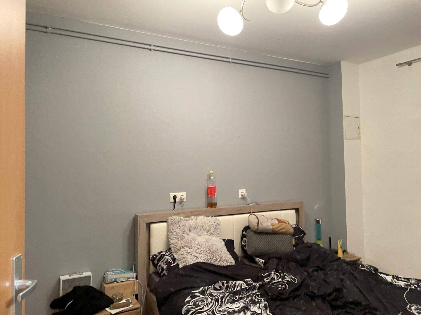 Schlafzimmer mit grau gestrichener Wand, Doppelbett und einfacher Einrichtung.