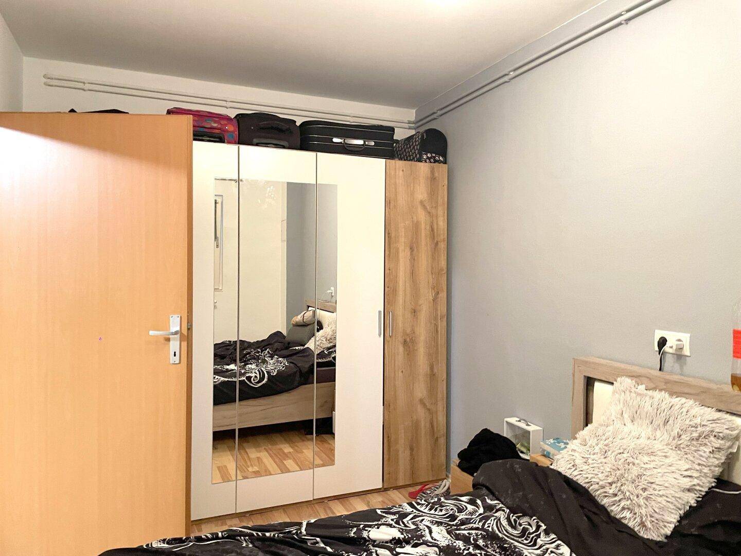 Schlafzimmer mit großem Spiegelschrank, Holzboden und einem Doppelbett.