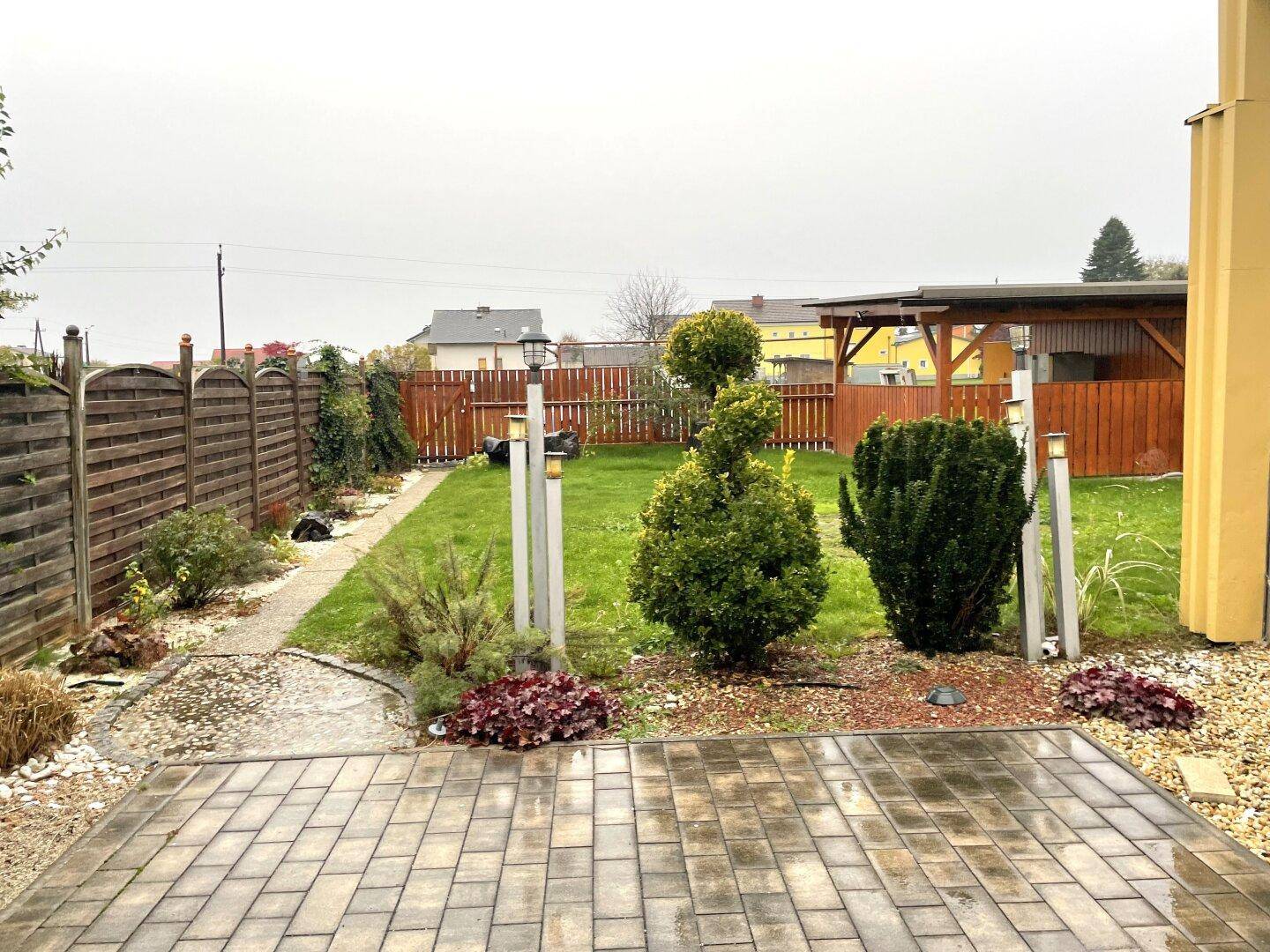 Gepflegter Garten mit Rasenfläche, gepflastertem Bereich und Holzzaun.