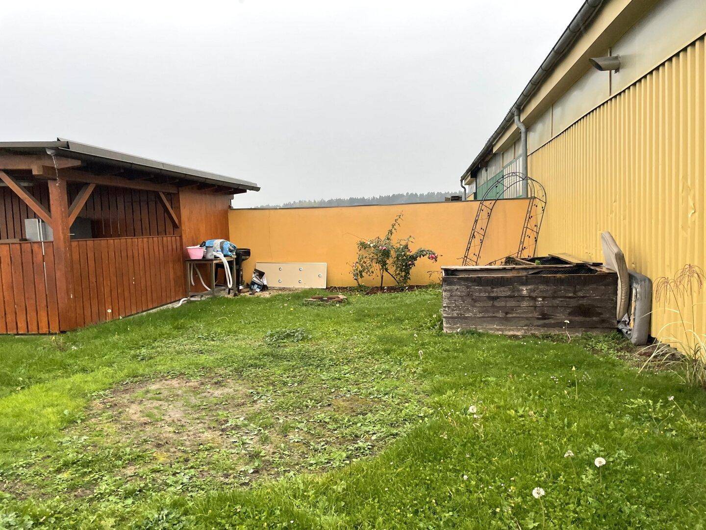 Hinterhof mit Rasenfläche, Holzschuppen und einem Hochbeet.