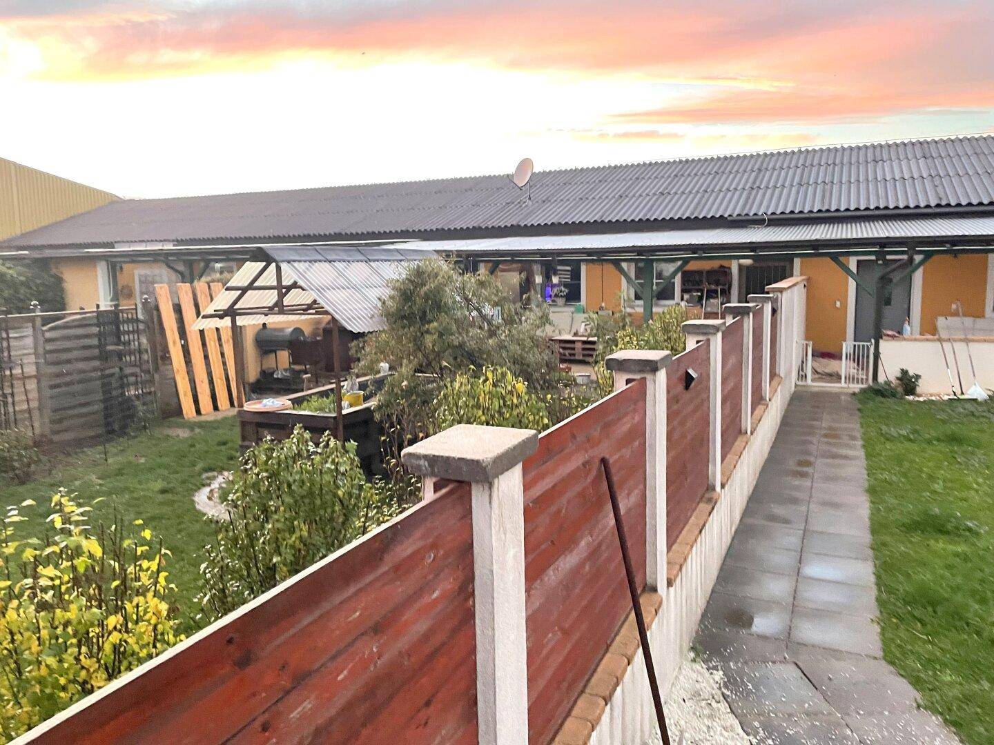 Garten mit Holzzaun, Rasenfläche und Blick auf die Rückseite des Hauses mit verschiedenen Anbauten.