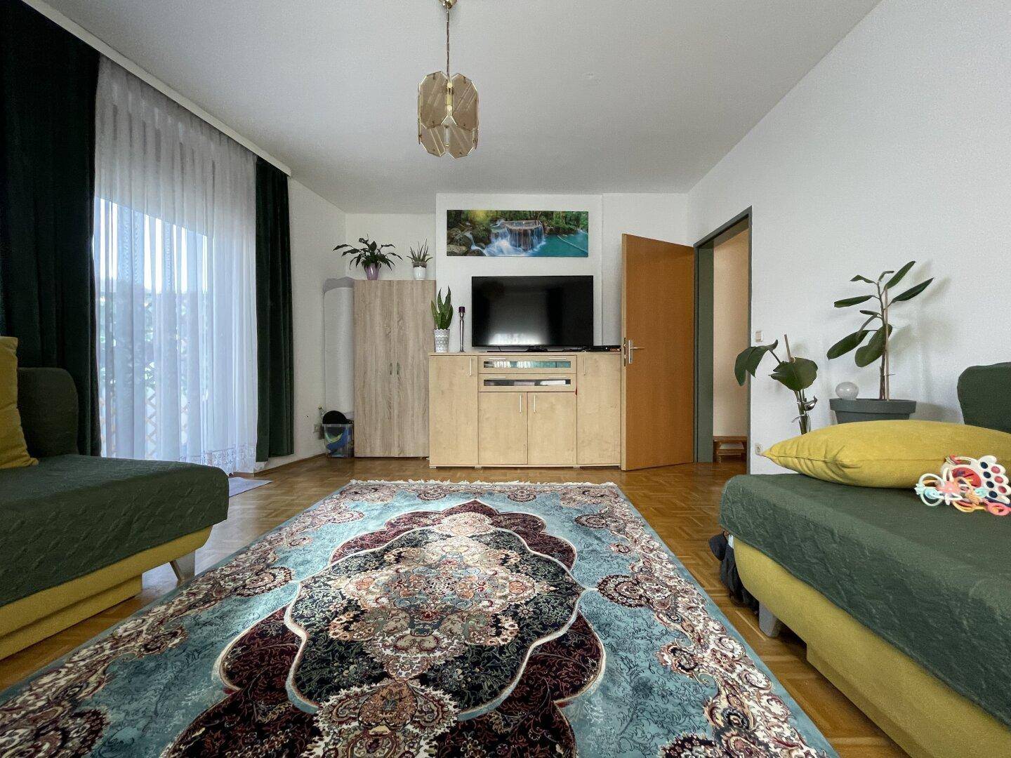 Geräumiges Wohnzimmer mit zwei grünen Sofas, großem Teppich und Zugang zum Balkon.