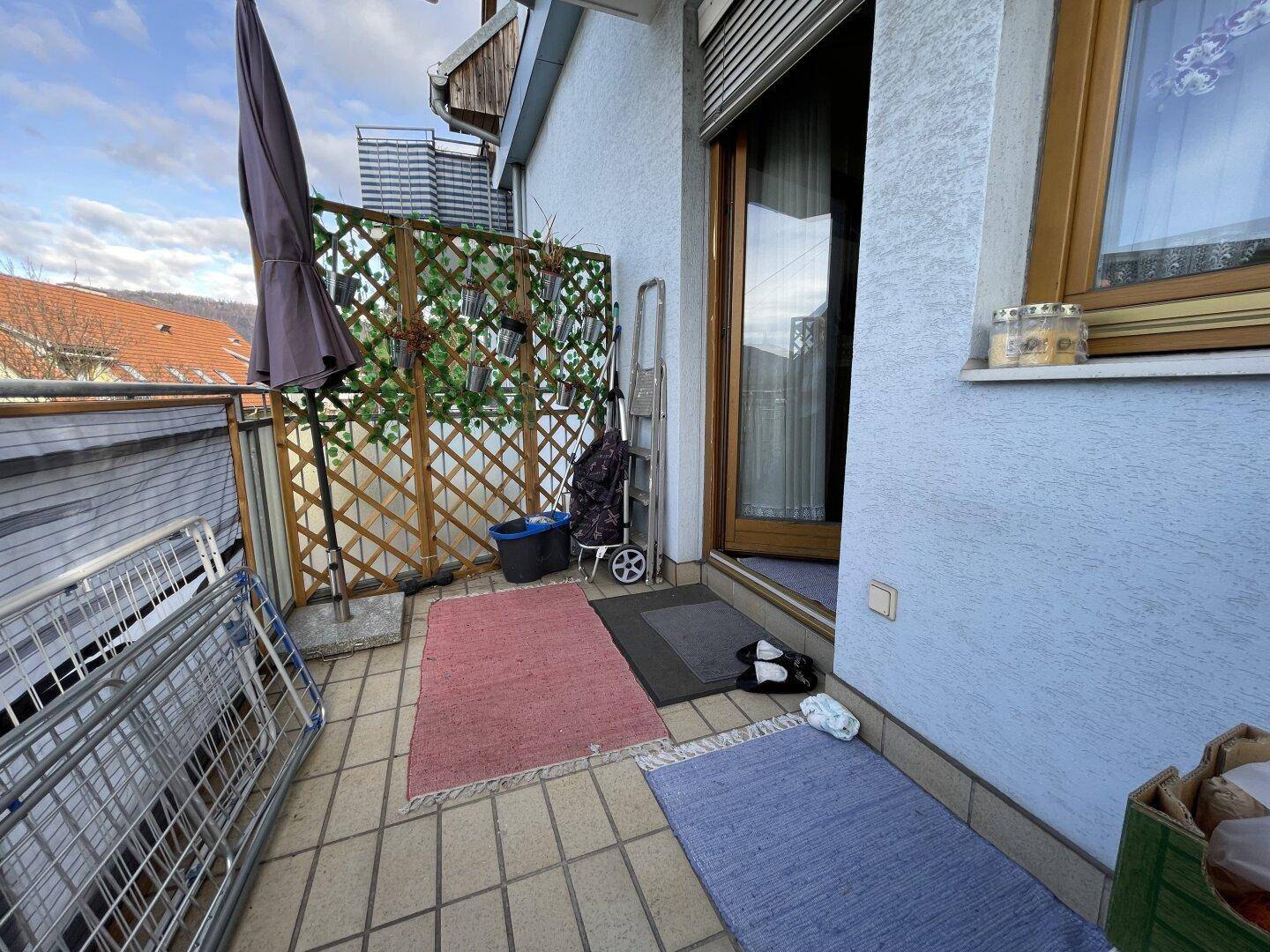 Kleiner Balkon mit Fliesenboden, Wäscheständer und Sichtschutz.