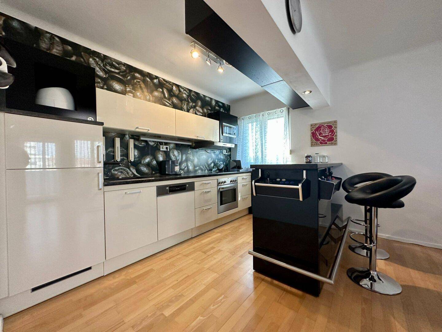 Moderne Küche mit beigen Hochglanzfronten, Holzboden und einer Frühstücksbar mit Hockern.