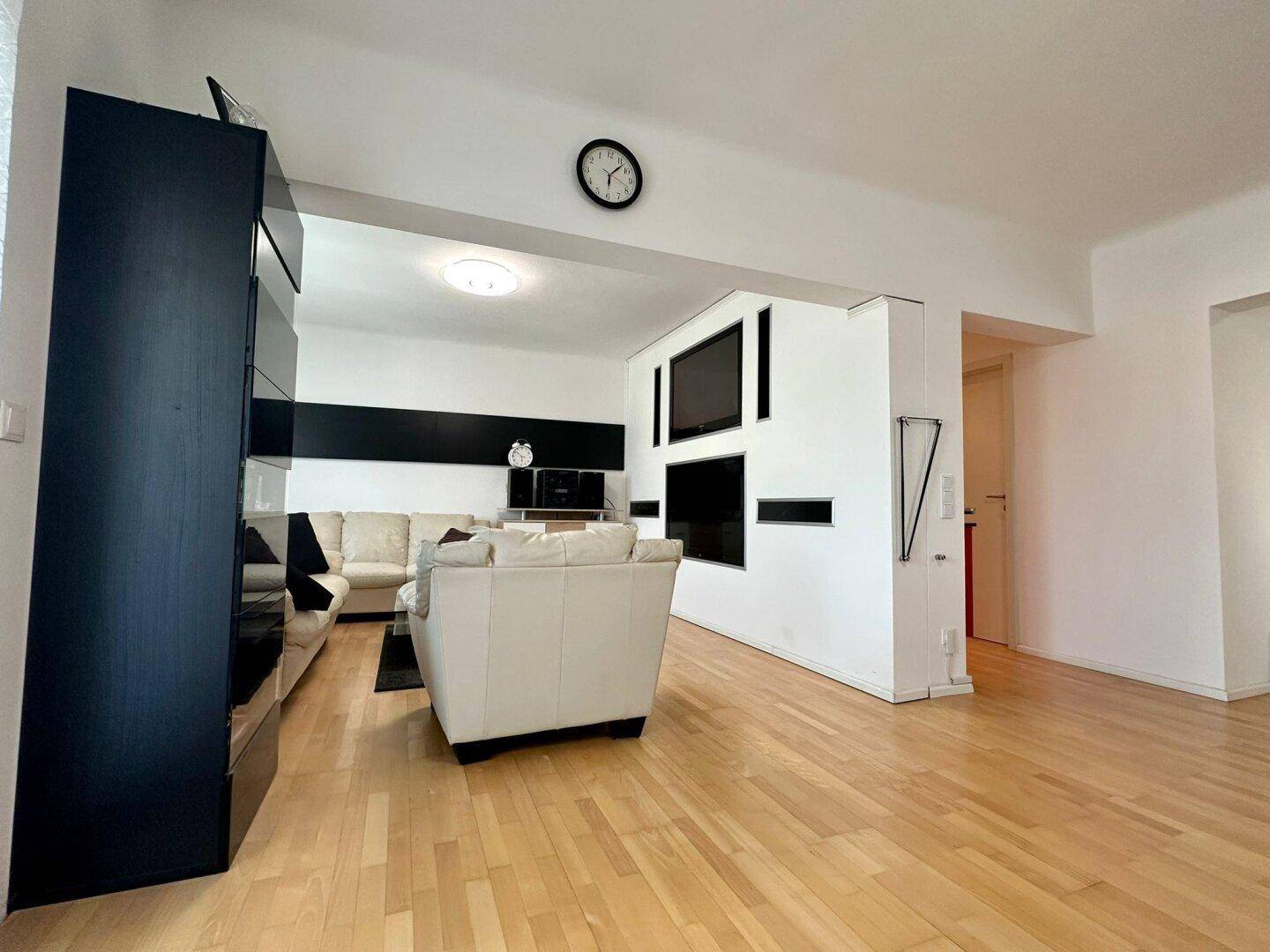 Geräumiges Wohnzimmer mit hellem Parkettboden, beigen Sofas und integriertem TV-Bereich.