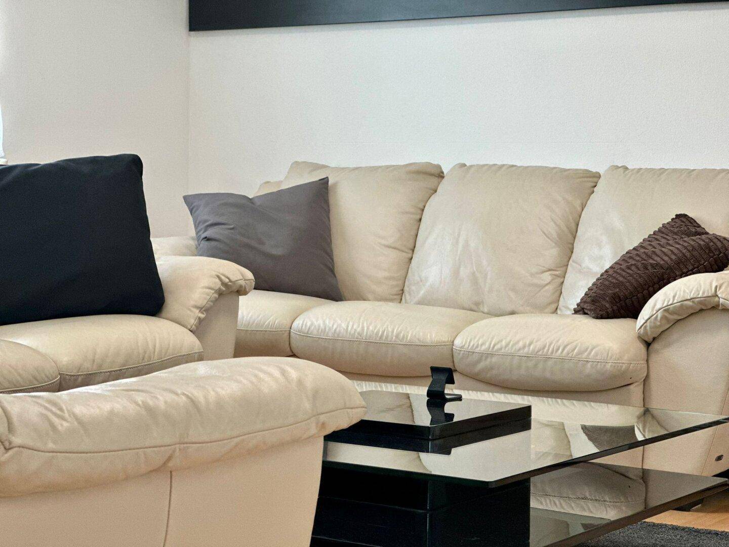 Beiges Ledersofa mit dunklen Kissen und einem modernen Couchtisch aus Glas und Schwarz.