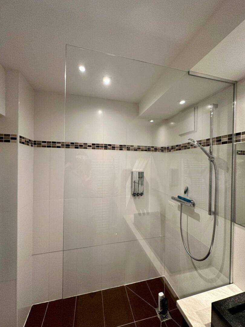 Duschbereich im Badezimmer mit Glasabtrennung, weißen Fliesen und moderner Duscharmatur.