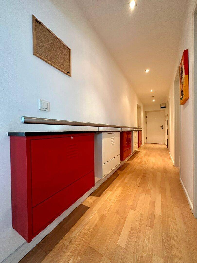 Heller Flur mit Holzparkettboden und modernen roten und weißen Schränken an der Wand.