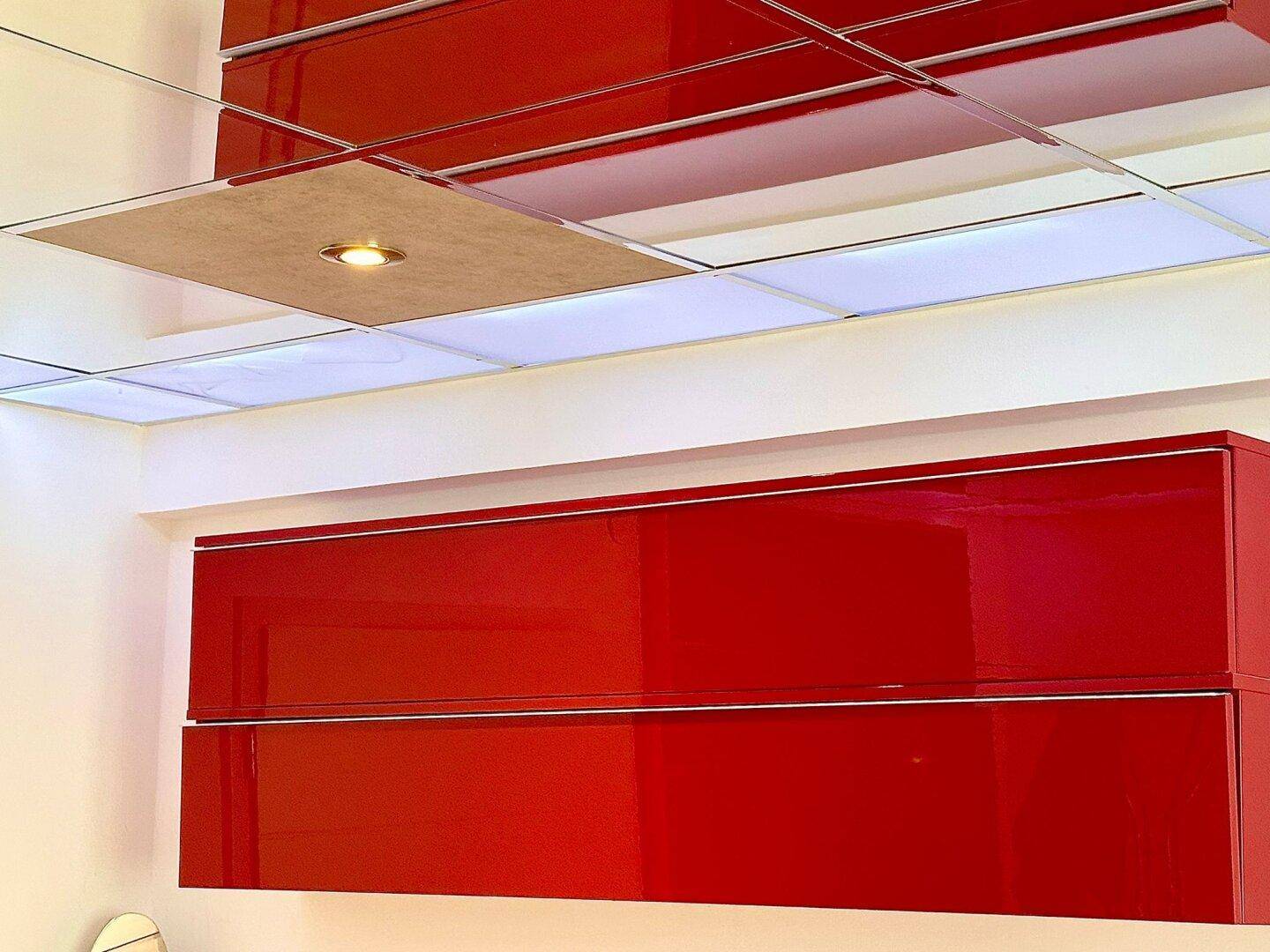 Detailansicht der Spiegelfliesendecke und eines roten Hochglanzschranks im Schlafzimmer.