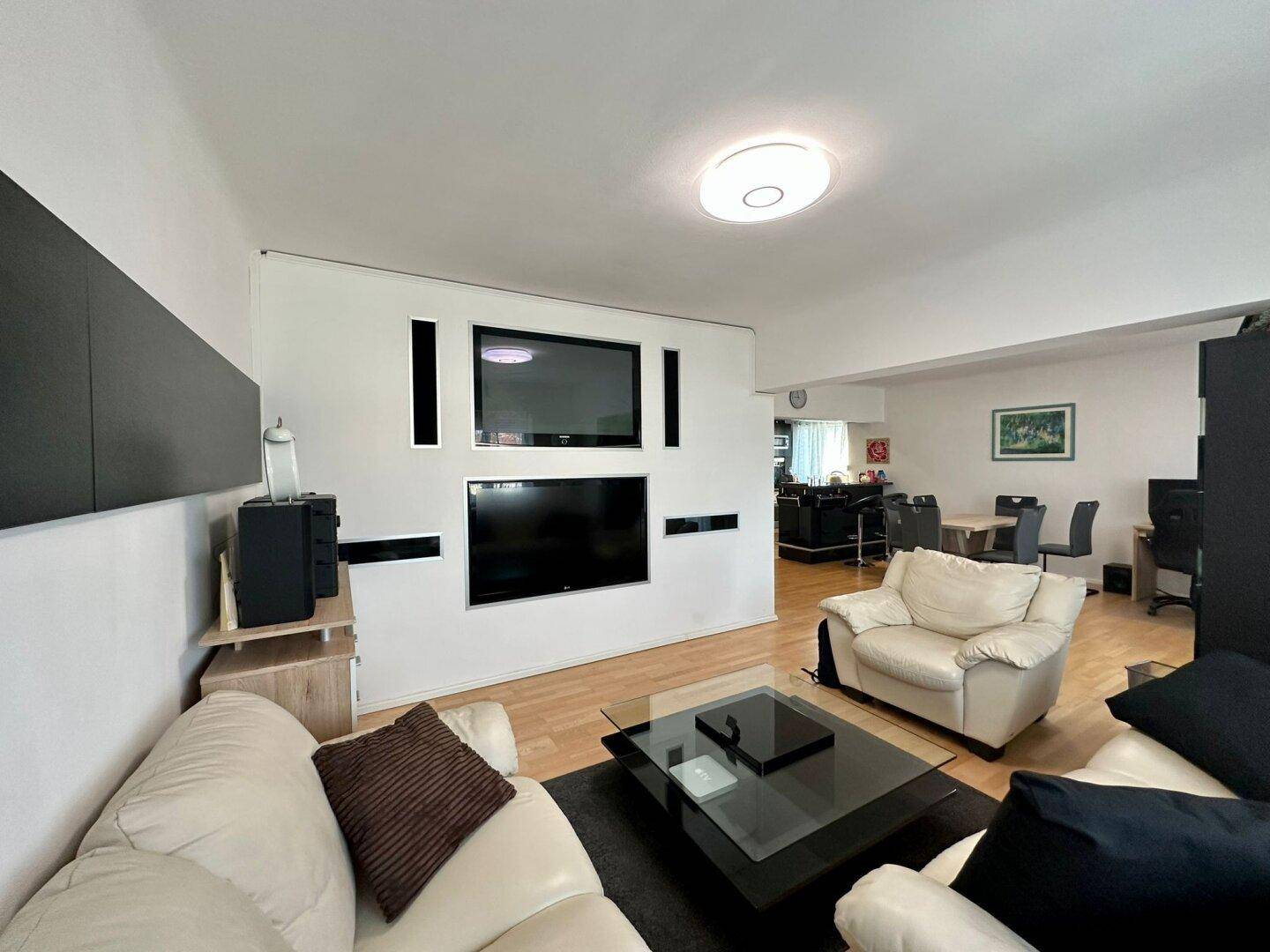 Offener Wohnbereich mit beigen Ledersofas, Couchtisch und Blick auf den Essbereich im Hintergrund.
