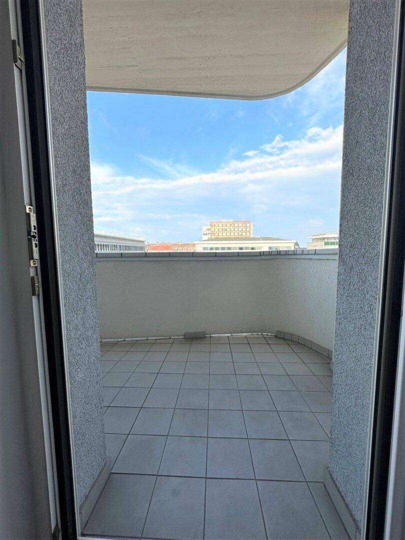 Blick vom Innenraum auf den gefliesten Balkon mit Stadtblick unter blauem Himmel.
