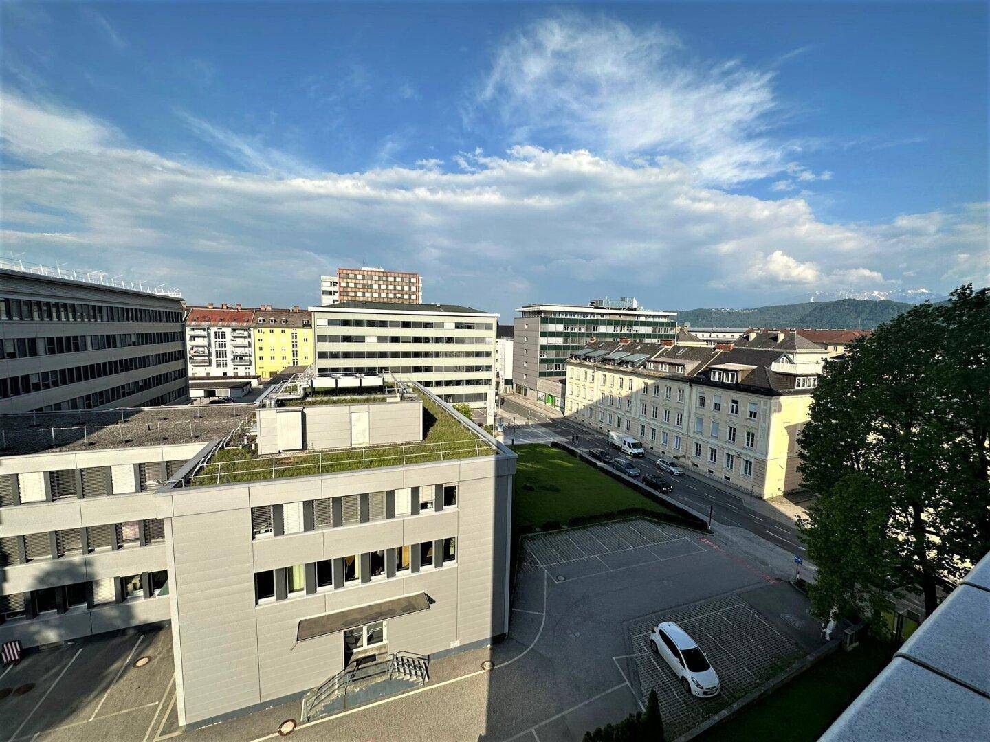 Weitläufiger Blick über die städtische Umgebung mit Gebäuden und grünen Dächern unter blauem Himmel.