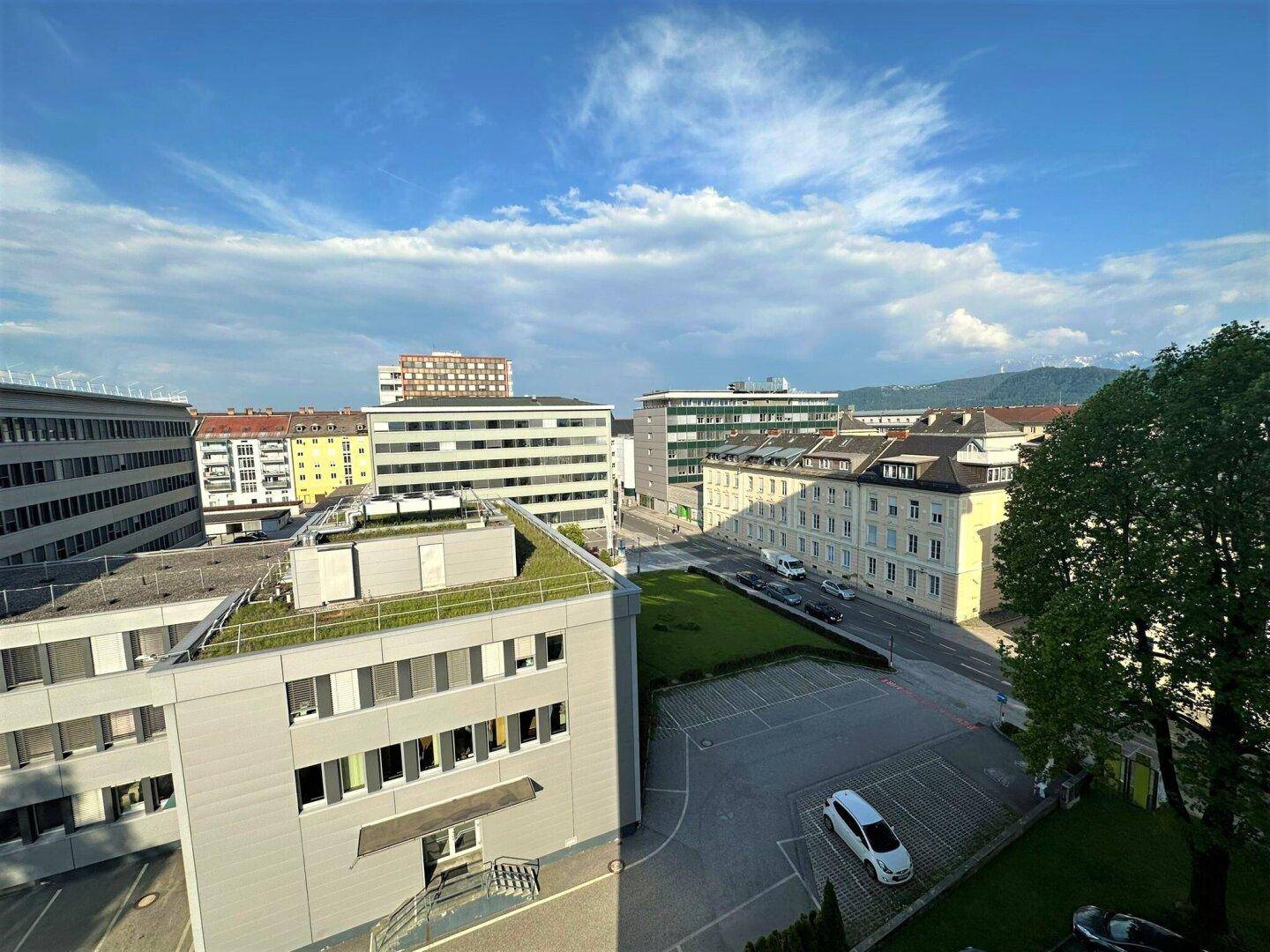 Weitläufiger Blick über die städtische Umgebung mit Gebäuden und grünen Dächern unter blauem Himmel.
