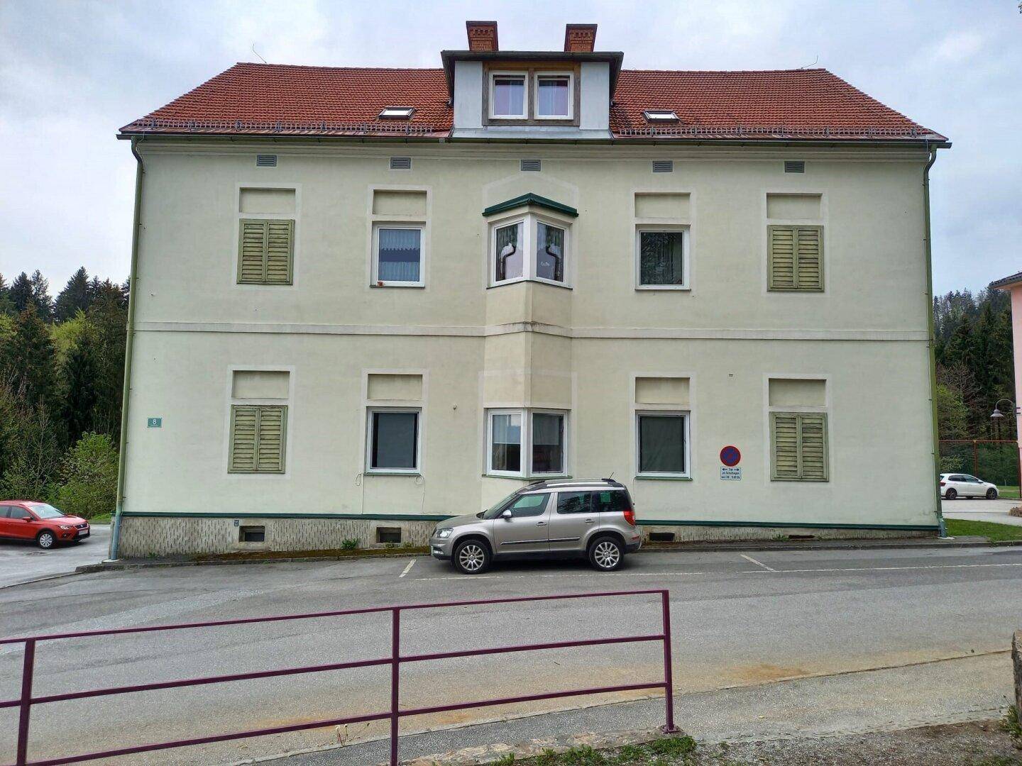 Vorderansicht des Gebäudes mit Erkerfenster, roten Dachziegeln und grünen Fensterläden.