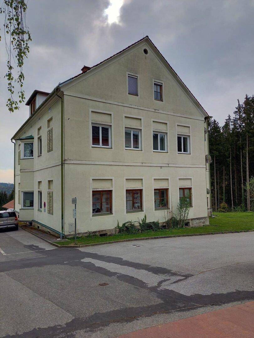 Seitenansicht des Gebäudes mit Blick auf die umliegende Landschaft und den Wald im Hintergrund.