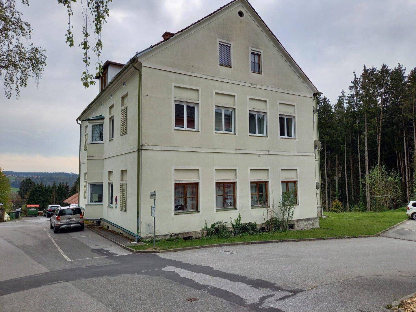 Ansicht des Gebäudes von der Straßenseite mit umliegender Natur und Wald im Hintergrund.