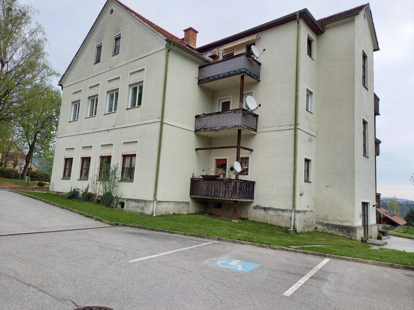 Rückseite des Gebäudes mit mehreren Balkonen und einem Behindertenparkplatz im Vordergrund.