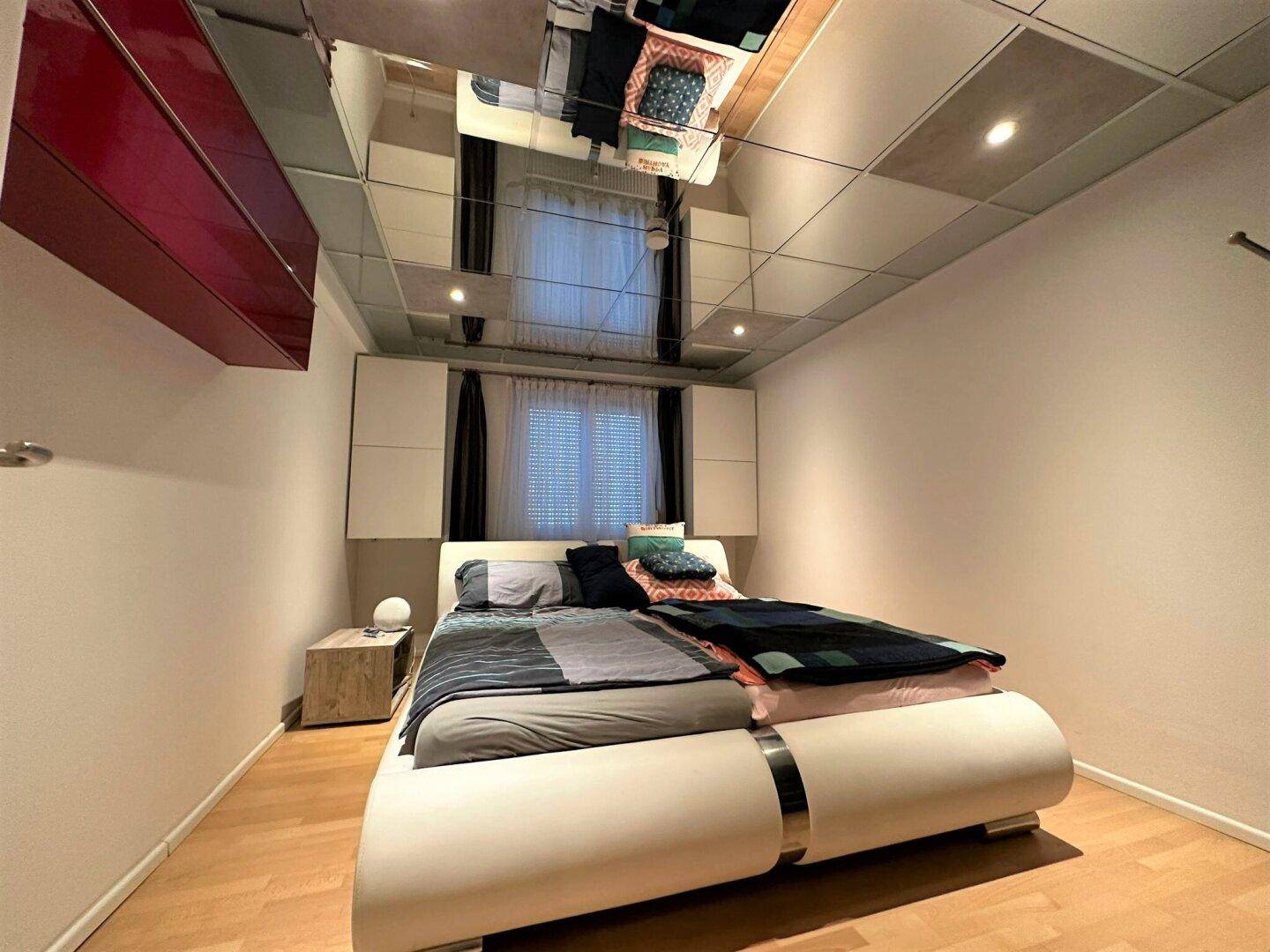 Schlafzimmer mit Doppelbett, Holzparkettboden und einer auffälligen Spiegelfliesendecke.
