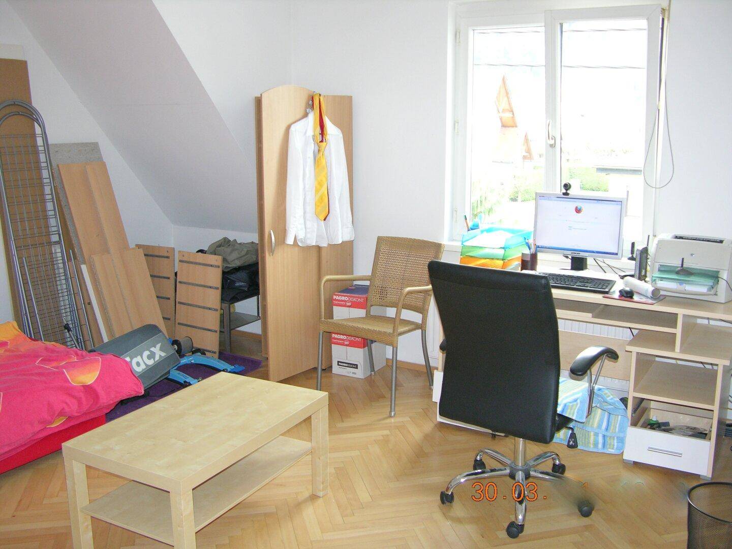 Dachzimmer mit Schreibtisch, Computer und Bett, gekennzeichnet durch eine Dachschräge.