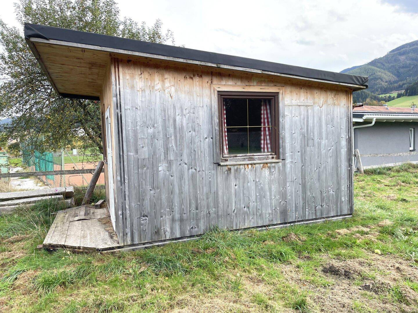 Rustikales Holzgartenhaus mit Pultdach und kleinem Fenster auf einer Grünfläche.