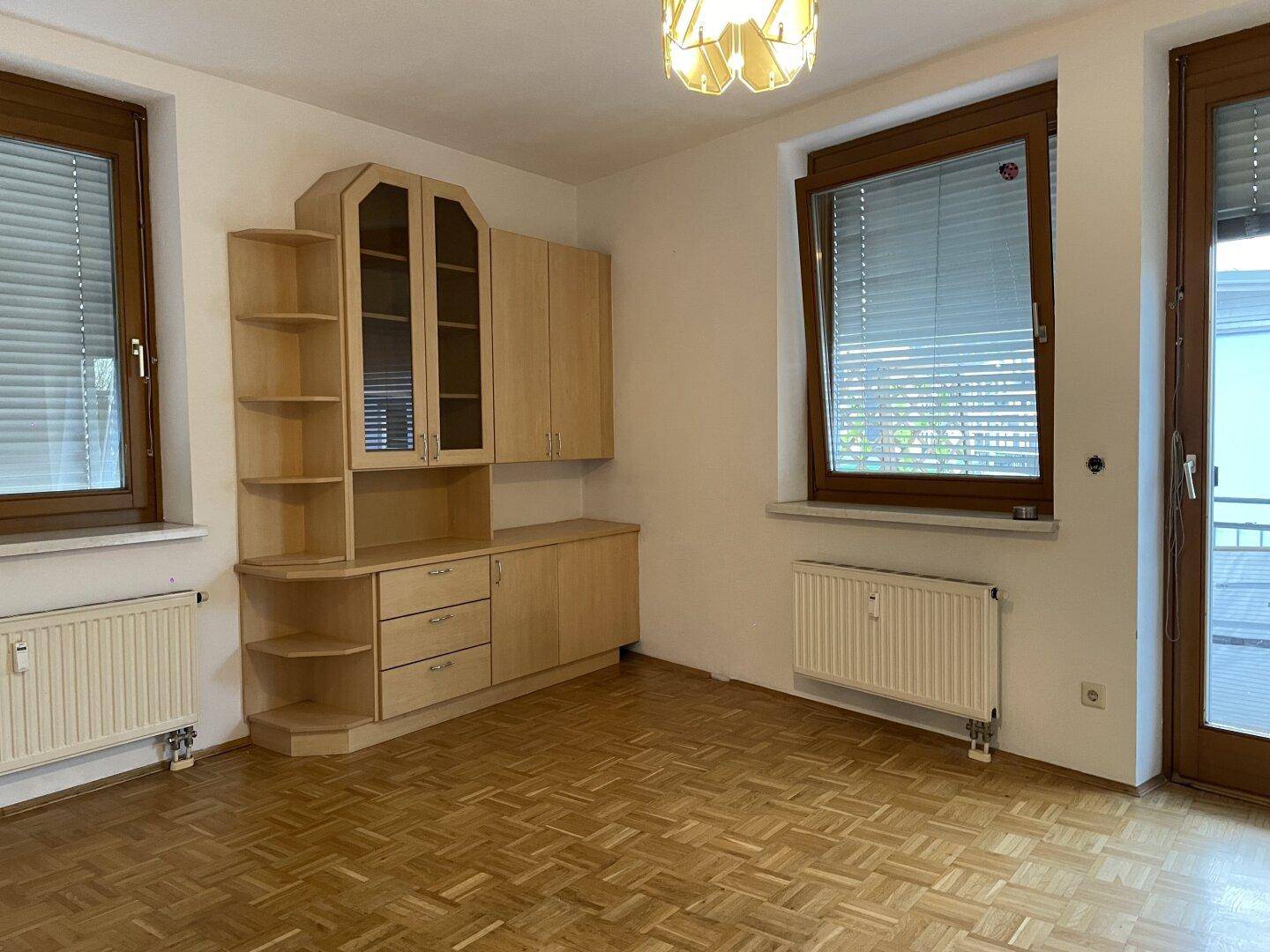 Heller Wohnraum mit Parkettboden, großen Fenstern und einem Einbauschrank.