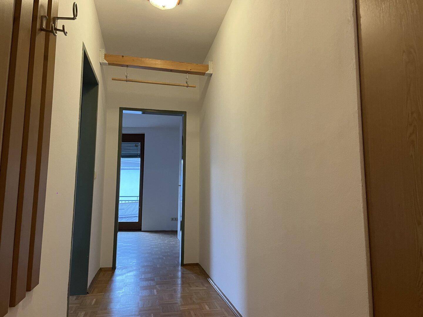 Schmaler Flur mit Parkettboden und Garderobe, der zu weiteren Räumen führt.