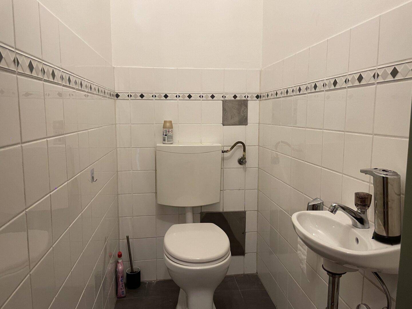 Gäste-WC mit weißen Fliesen, einem kleinen Waschbecken und einer Toilette.