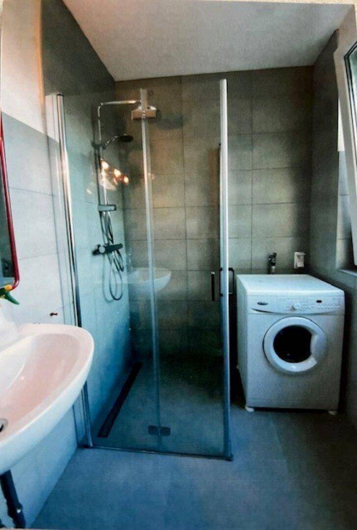 Modernes Badezimmer mit einer Duschkabine aus Glas, einem Waschbecken und einem Fenster für Tageslicht.