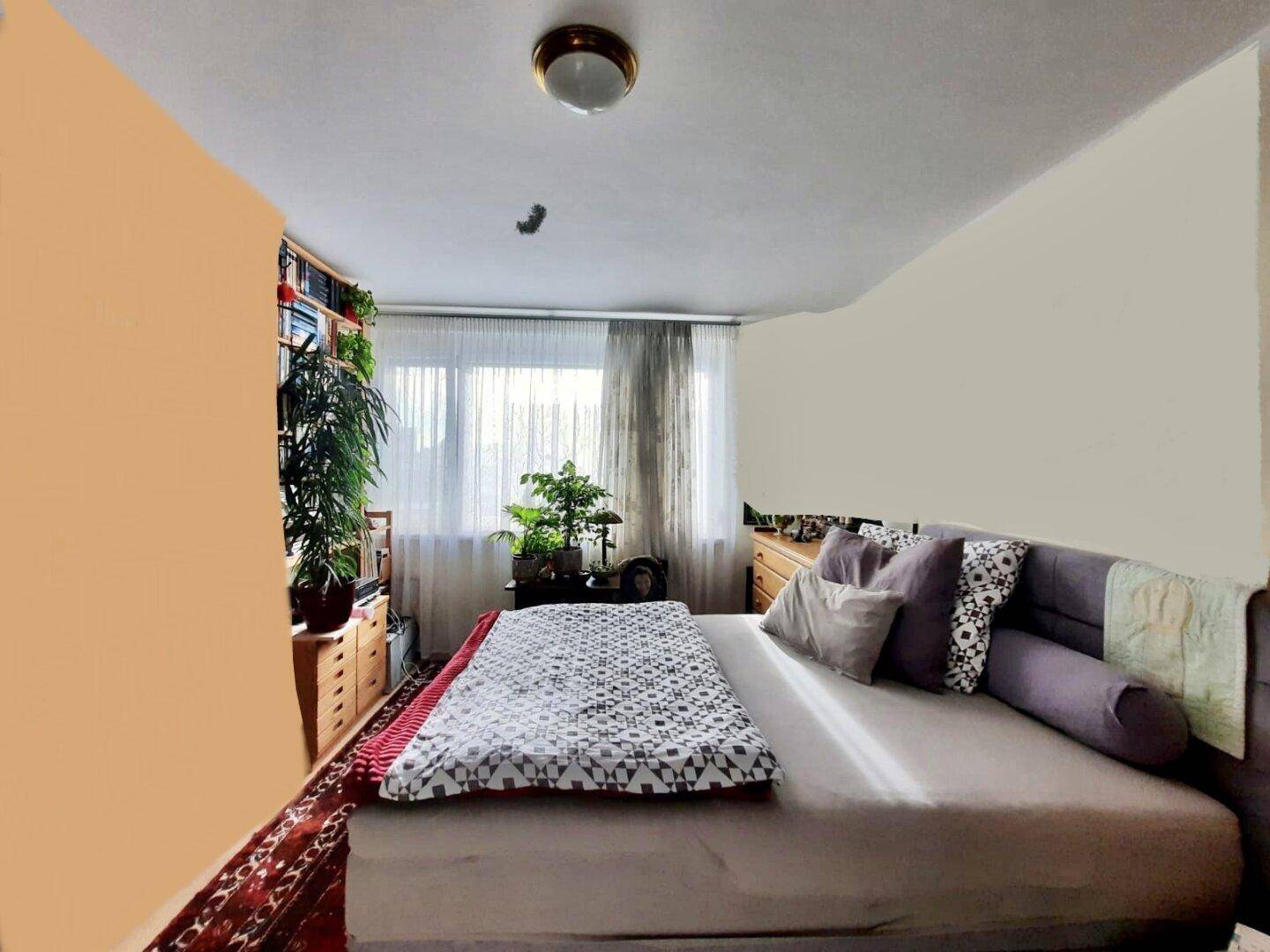 Helles Schlafzimmer mit großem Bett, Holzmöbeln und einem Fenster, das einen angenehmen Blick ins Grüne ermöglicht.